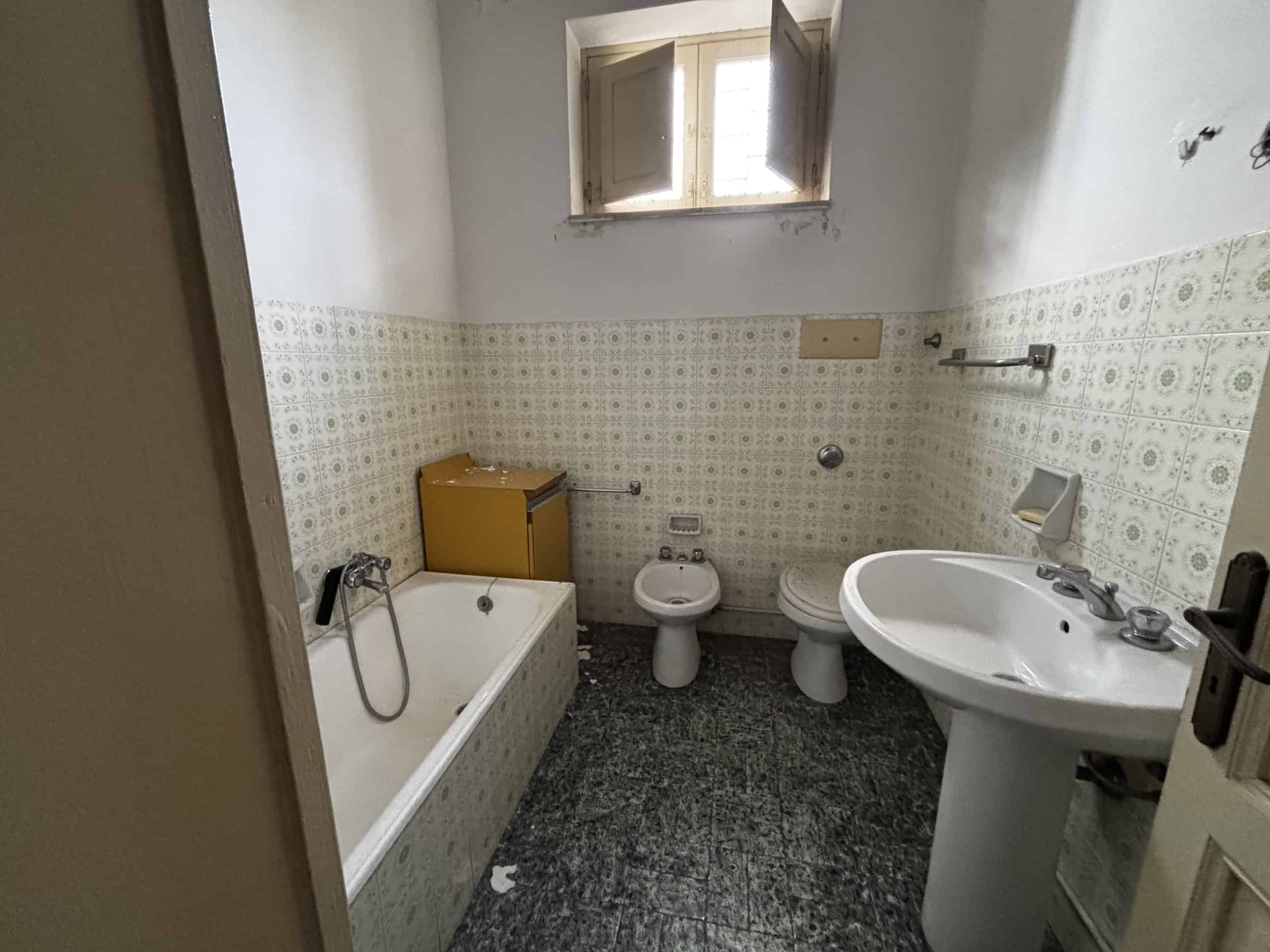 Bagno spazioso con vasca, bidet, lavabo e finestra, arredato in stile semplice, illuminato dalla luce naturale.