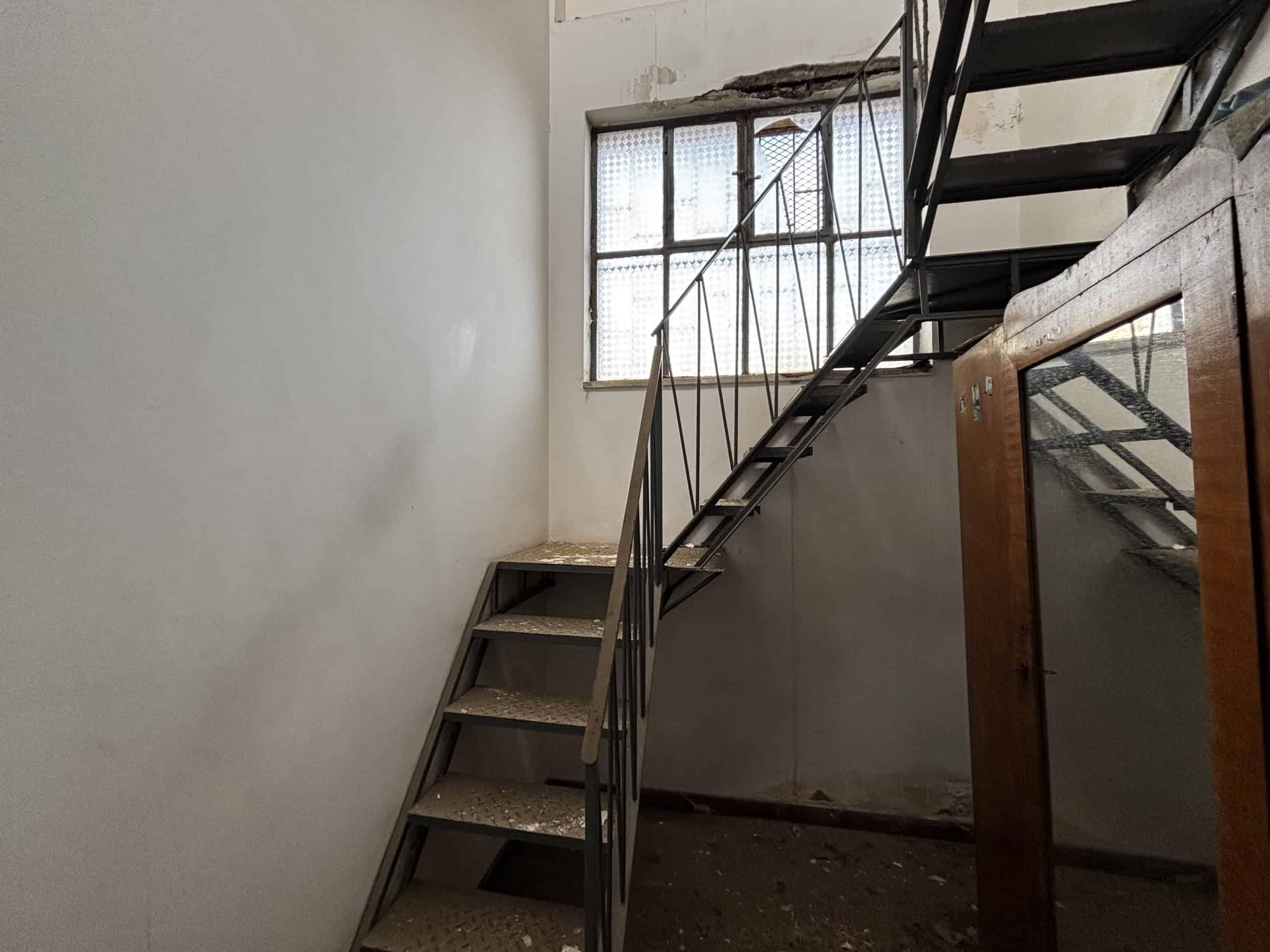 Scale interna con scala in metallo e gradini in legno, illuminata da una grande finestra con inferriate, in un ambiente di proprietà NextCasa.