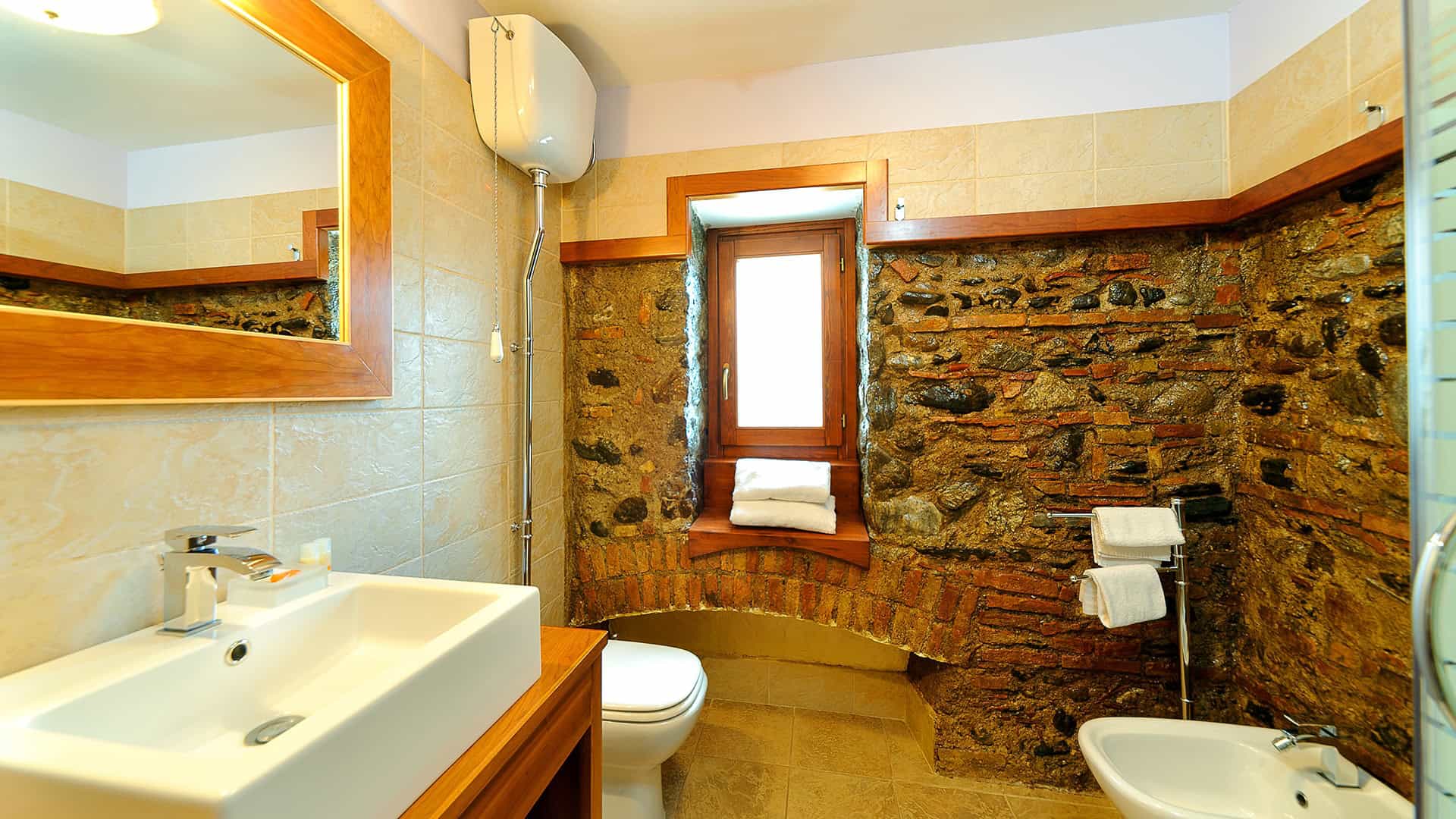 Lavabo e bagno con pareti in pietra e finestra, stile rustico, in un ambiente accogliente e ben illuminato.
