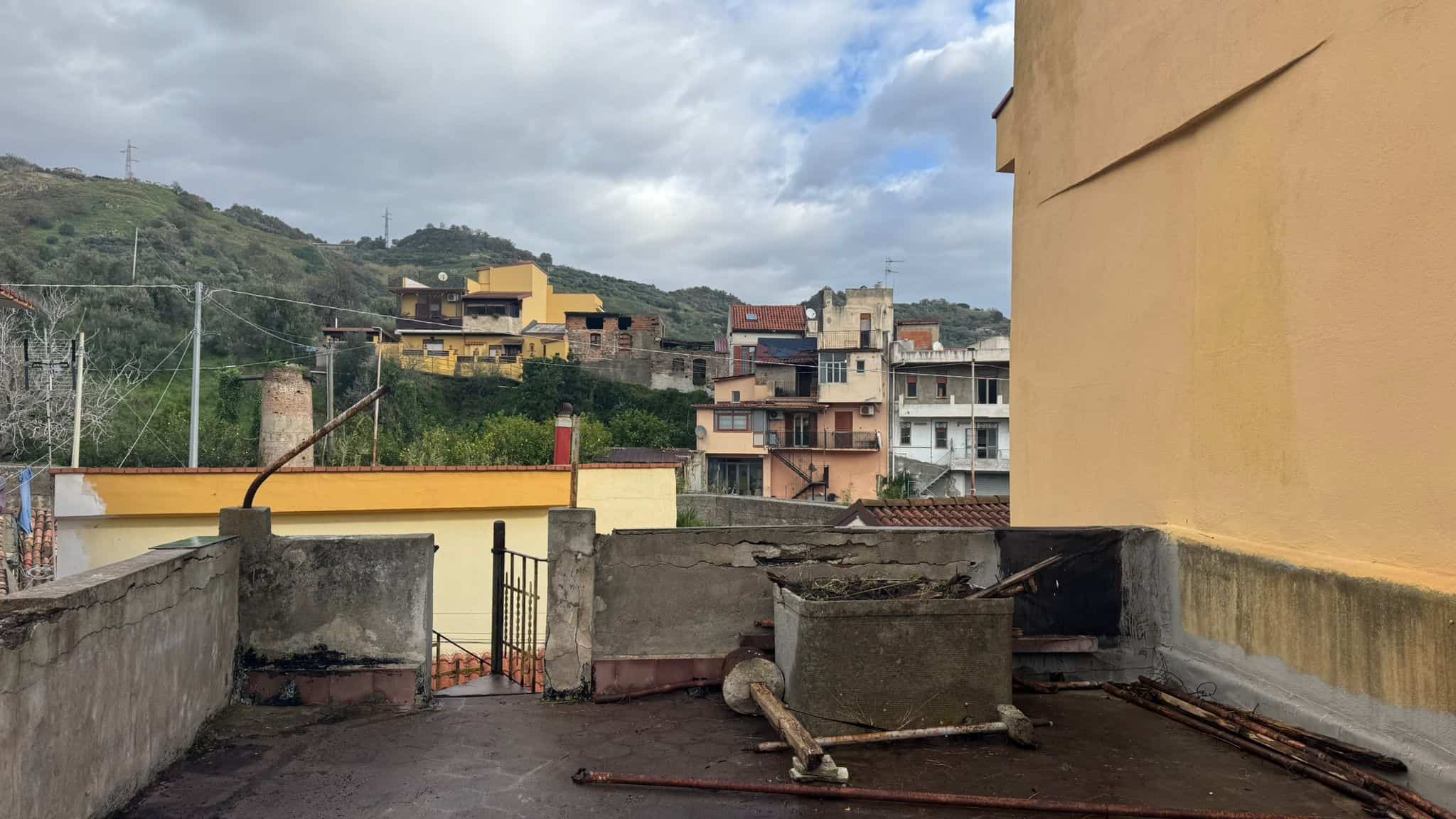 Tetto di un edificio residenziale con vista sulle colline e sui quartieri circostanti, in una giornata nuvolosa.