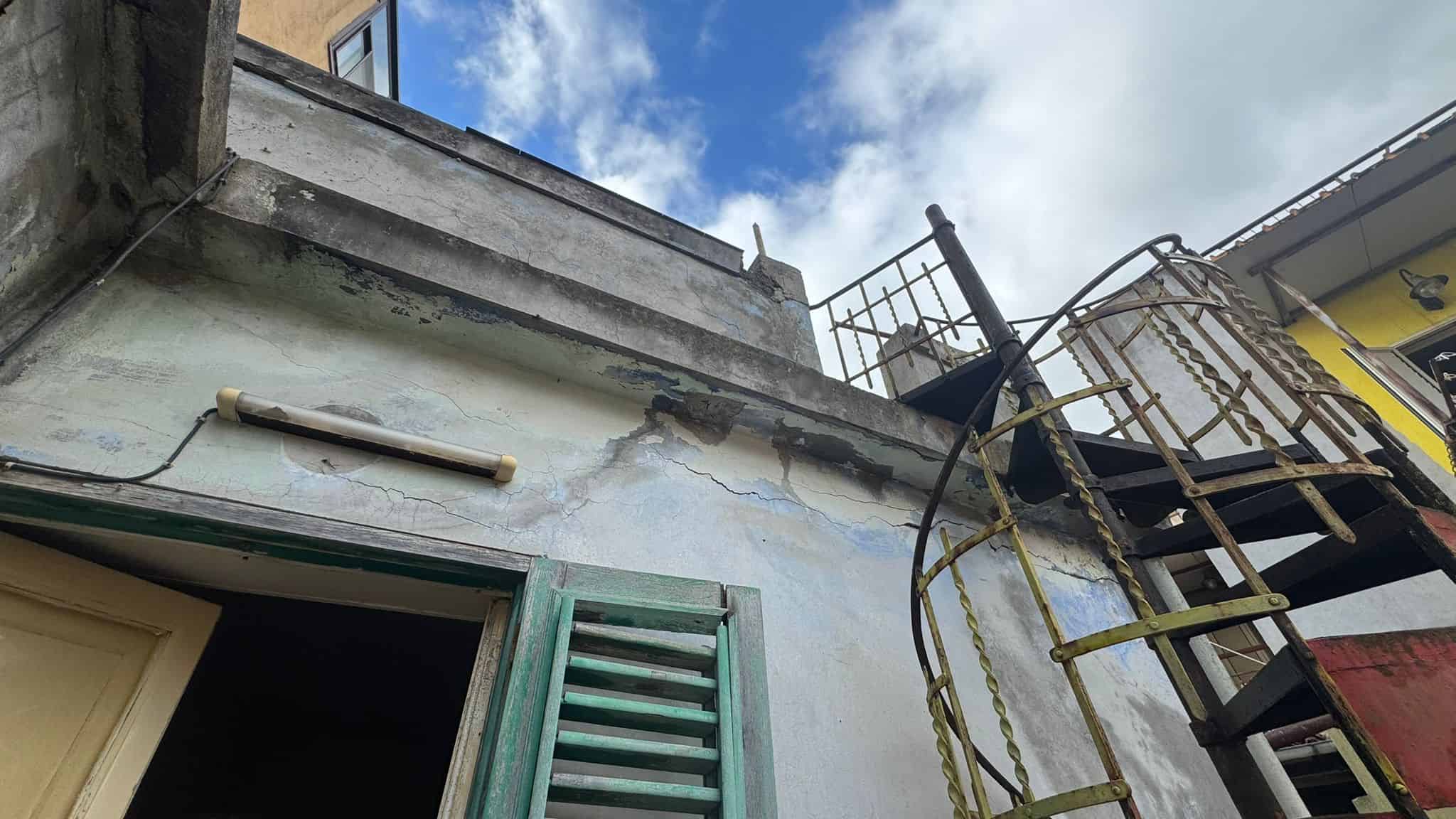 Esterno di un edificio in fase di ristrutturazione con ponteggio e scaffalature, vista verso il cielo con nuvole bianche e cielo blu.