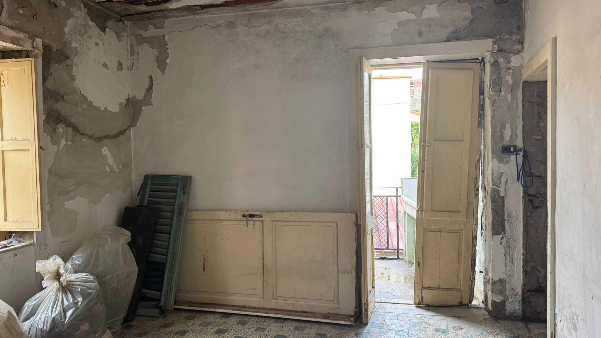 Vecchio interno di una casa in ristrutturazione con pareti in fase di restauro e porta aperta che conduce a un balcone, evidenziando lavori di ristrutturazione edilizia.