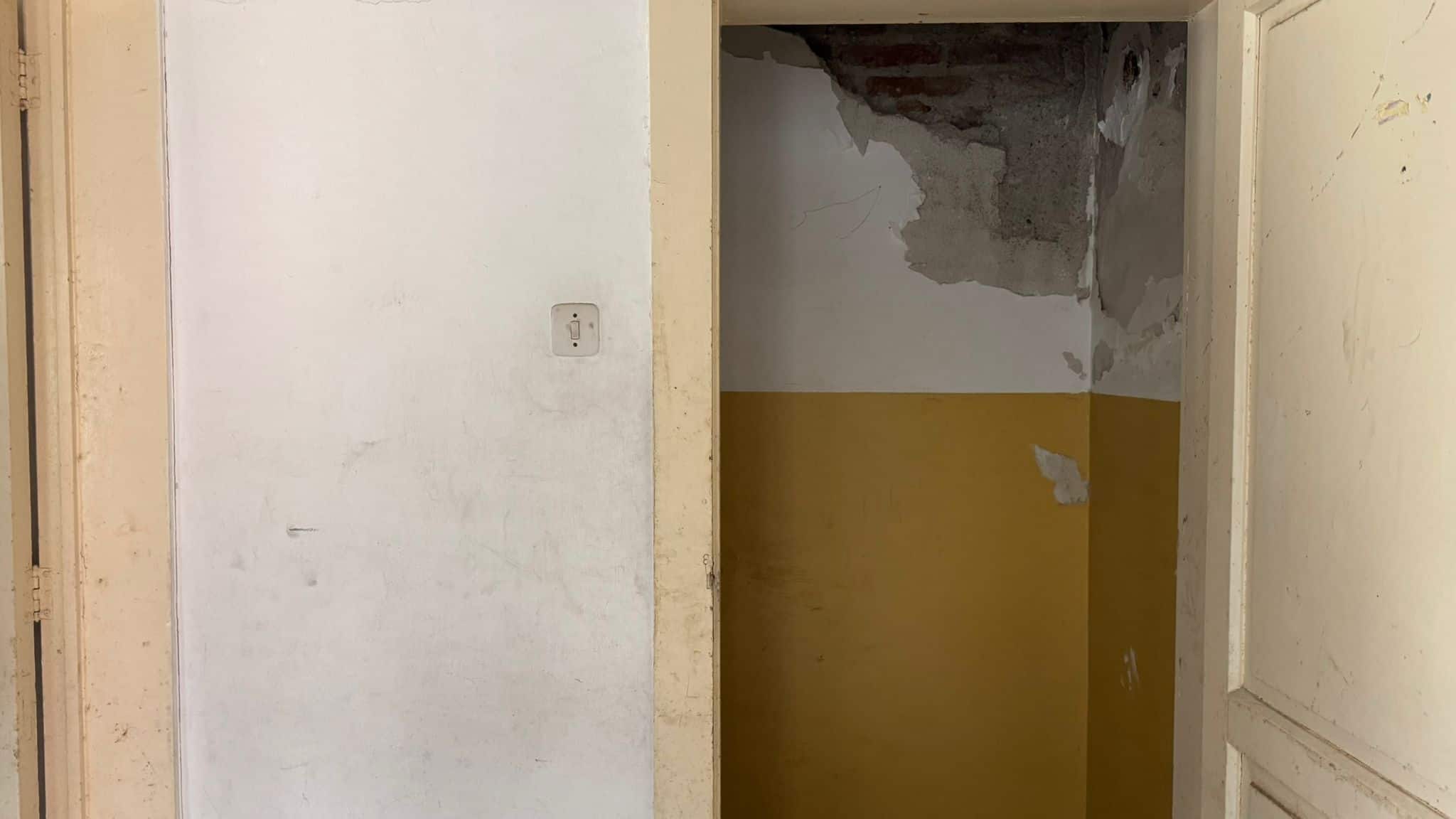 Immagine di un interno in fase di ristrutturazione con pareti dipinte in bianco e giallo, soffitto danneggiato e lavori di ristrutturazione in corso.