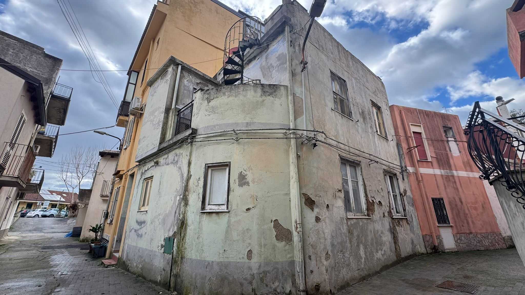 Vecchia casa in stile urbano con pareti usurate e dettagli architettonici caratteristici, situata in un quartiere residenziale. Edificio con pareti di colore chiaro e finestre piccole, sotto un cielo.