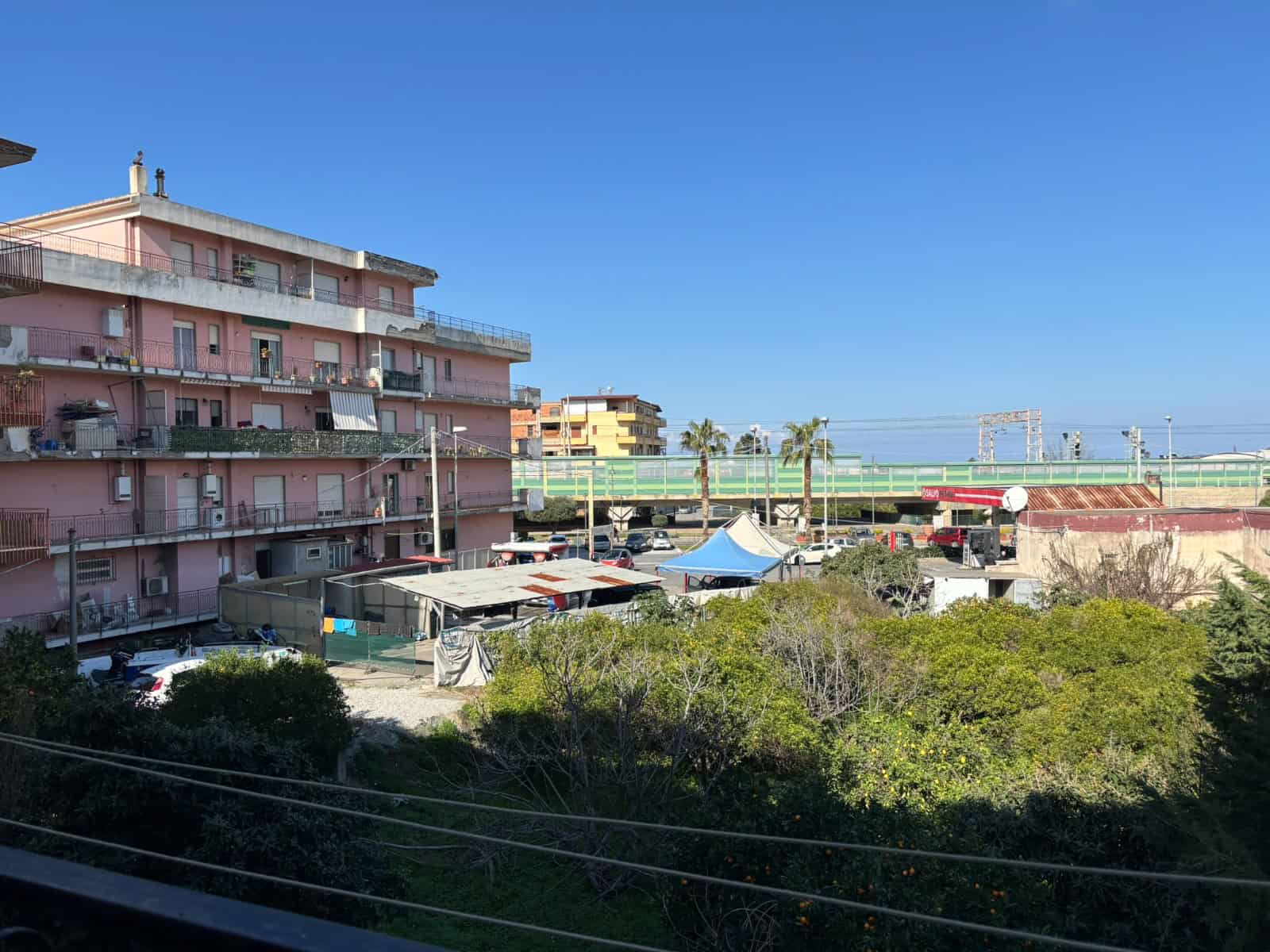 Balcone con vista su edifici residenziali e aree verdi, in una giornata soleggiata con cielo azzurro, in un quartiere urbano.