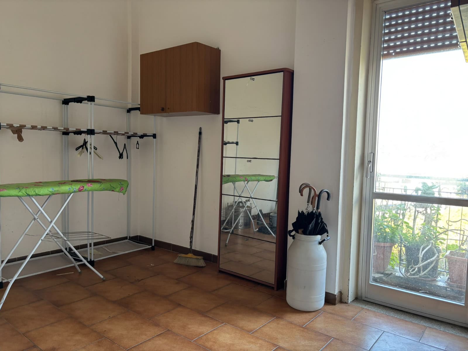 Asciugatrice in un ambiente domestico con accessori e mobili, illuminato dalla luce naturale proveniente da una porta finestra. Ideale per la cura dei capi di abbigliamento in casa.