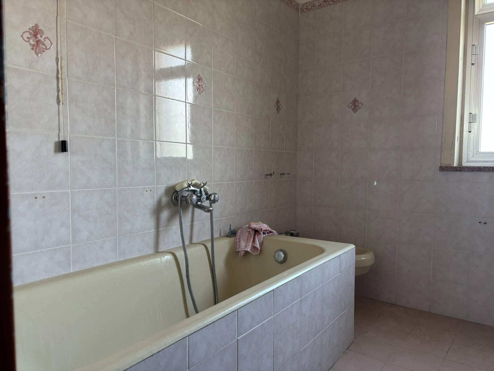 Doccia e vasca da bagno in un bagno spazioso con pareti rivestite di piastrelle beige e finestra che permette l'ingresso di luce naturale.