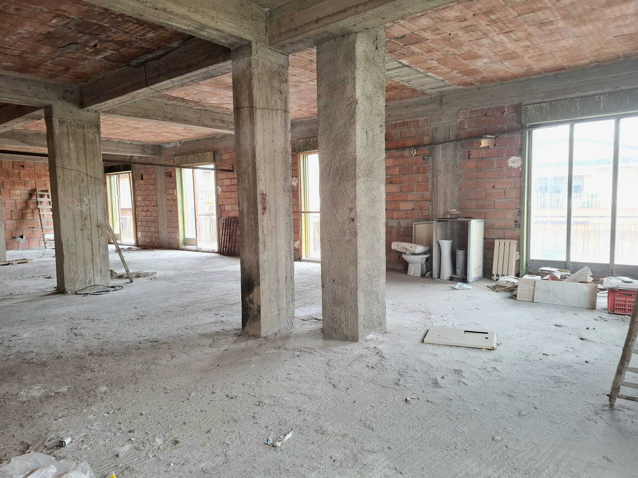 Interno di un edificio in costruzione con pareti in mattoni e colonne di cemento, spazio aperto e luminoso.