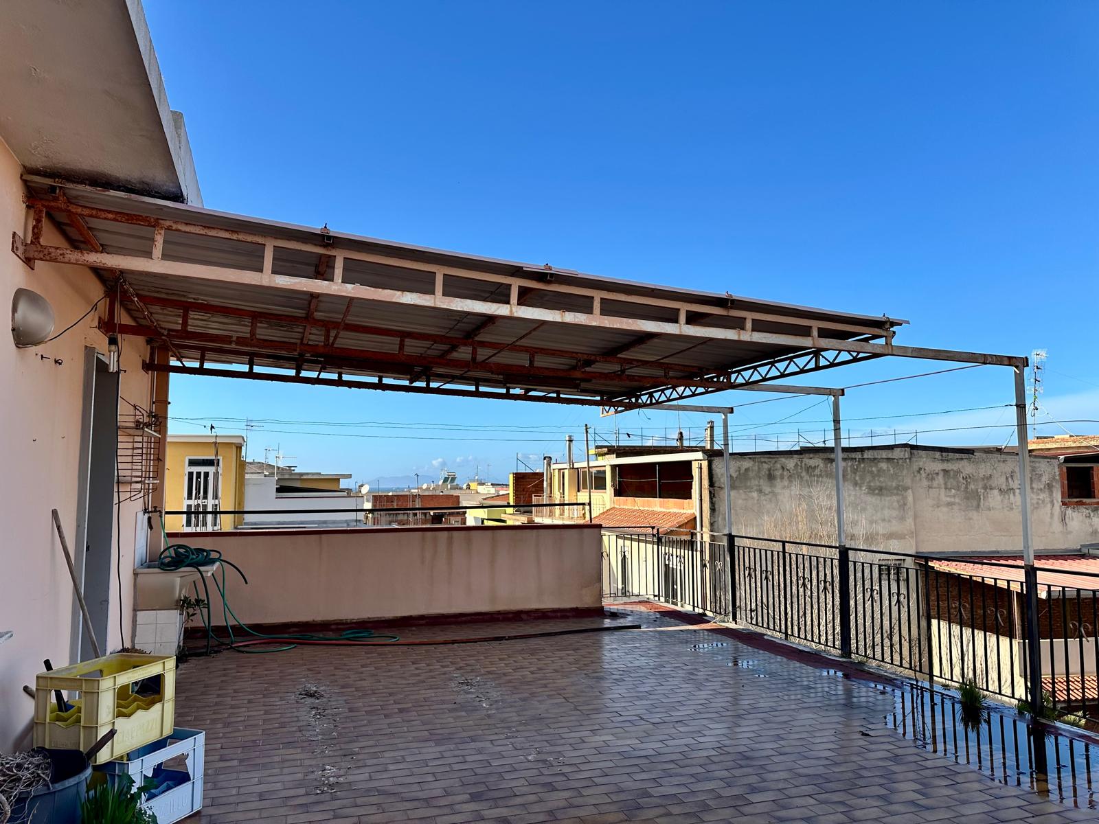 Tettoia in metallo e copertura in vetro su un ampio terrazzo urbano con vista su edifici residenziali, ideale per spazi esterni e relax all'aperto.