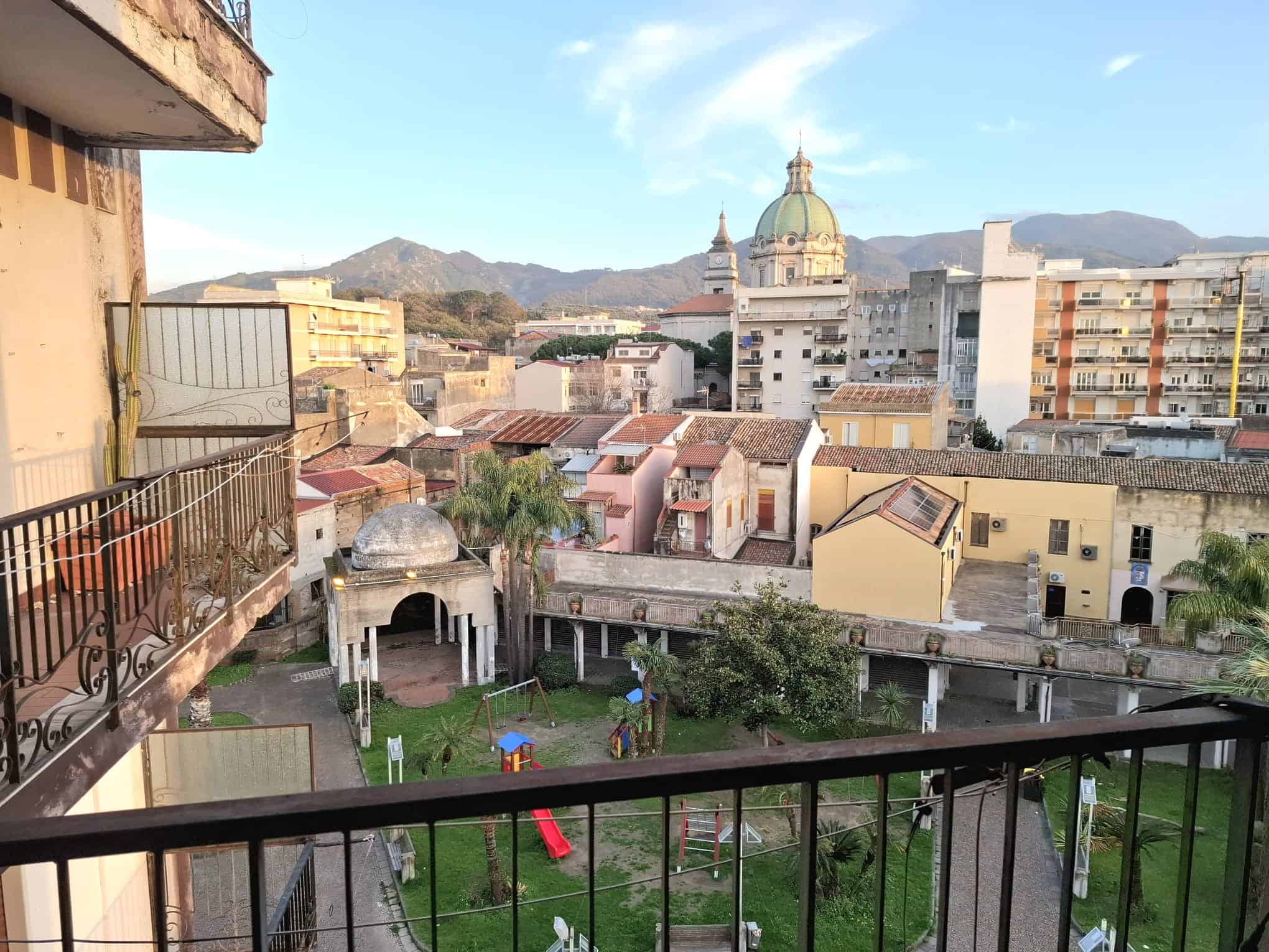 Balcone con vista sulla città e sul parco, con edifici storici e montagne sullo sfondo, in un ambiente urbano vivace e pittoresco, ideale per vivere o investire in immobili di pregio.