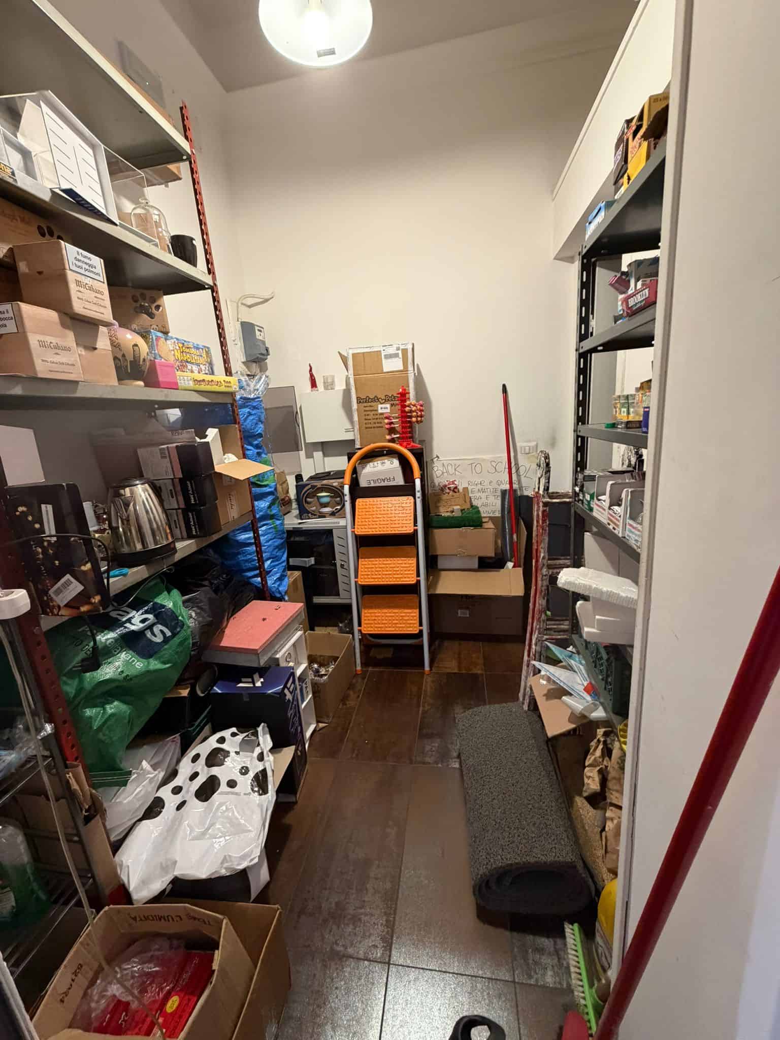 Scaffale di stoccaggio in un magazzino con vari prodotti, scatole e attrezzi, in un ambiente ben organizzato e illuminato.
