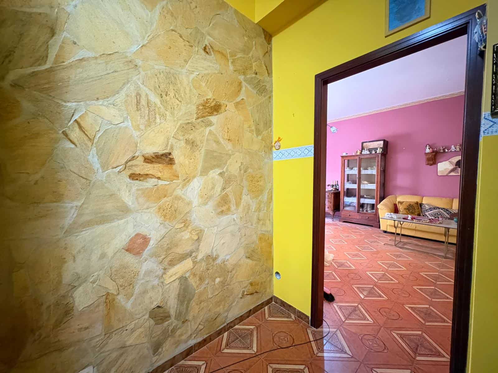Appartamento con parete in pietra naturale e ingresso a una zona soggiorno colorata, con pavimento in piastrelle geometriche e arredi vintage.