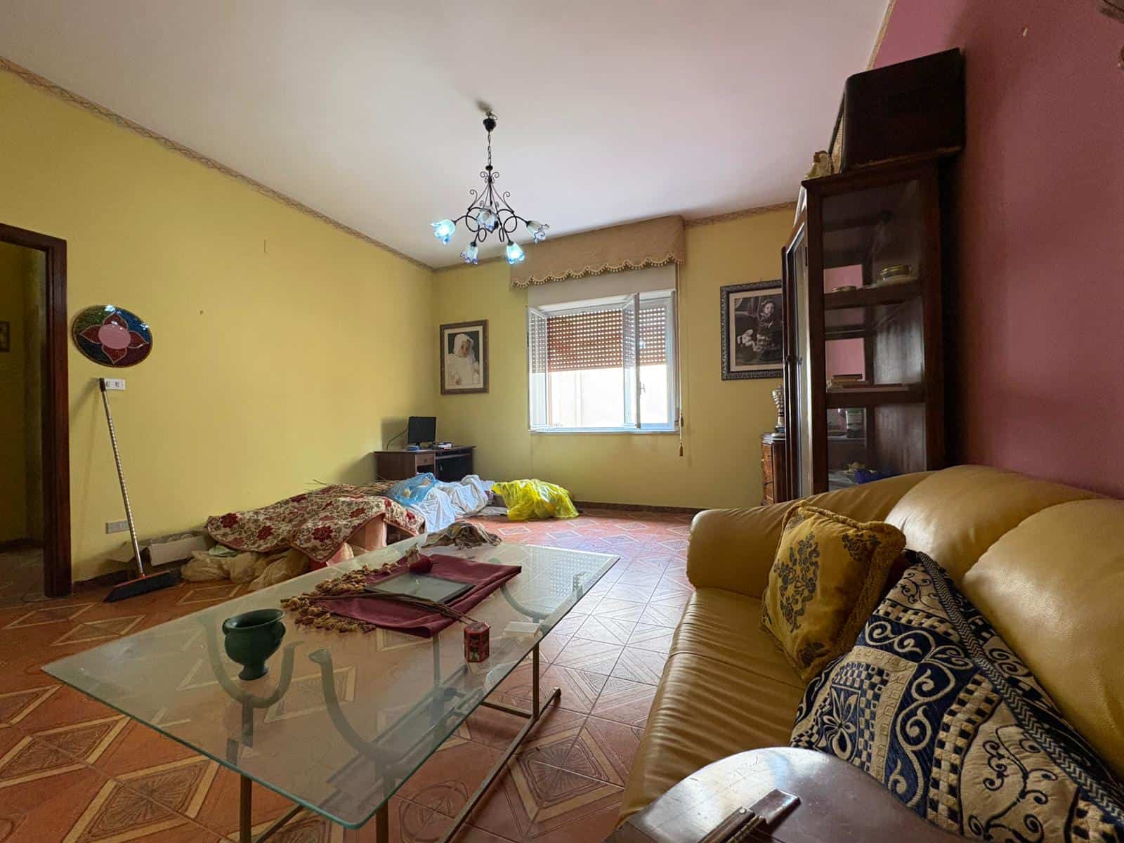 Interno soggiorno con divano beige, tavolo in vetro, pareti colorate e decorazioni, luce naturale dalla finestra, stile abitativo accogliente e luminoso.
