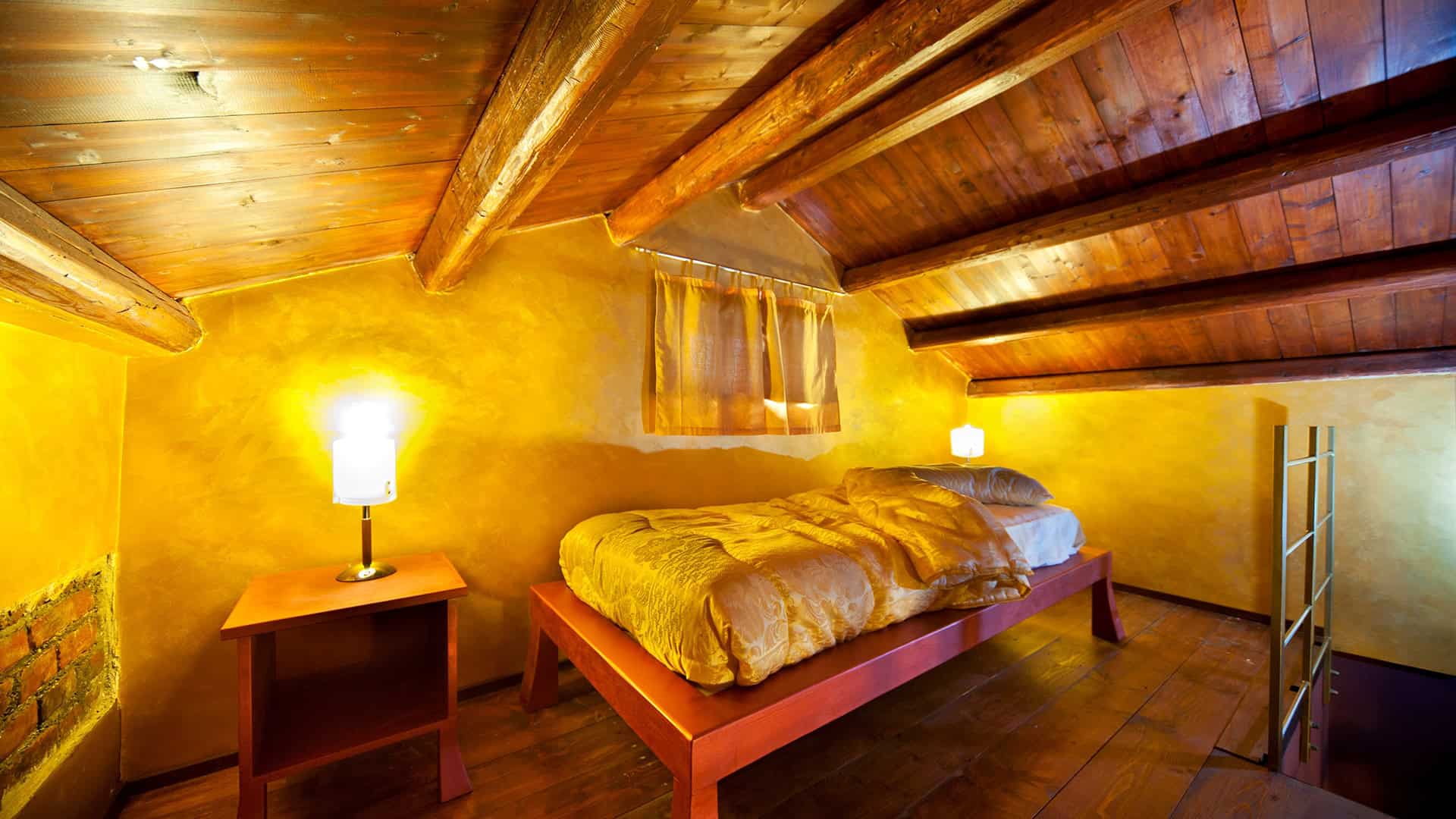 Ampio soggiorno in stile rustico con soffitto in legno e pareti gialle, letto matrimoniale e illuminazione calda, ideale per un ambiente accogliente e confortevole.