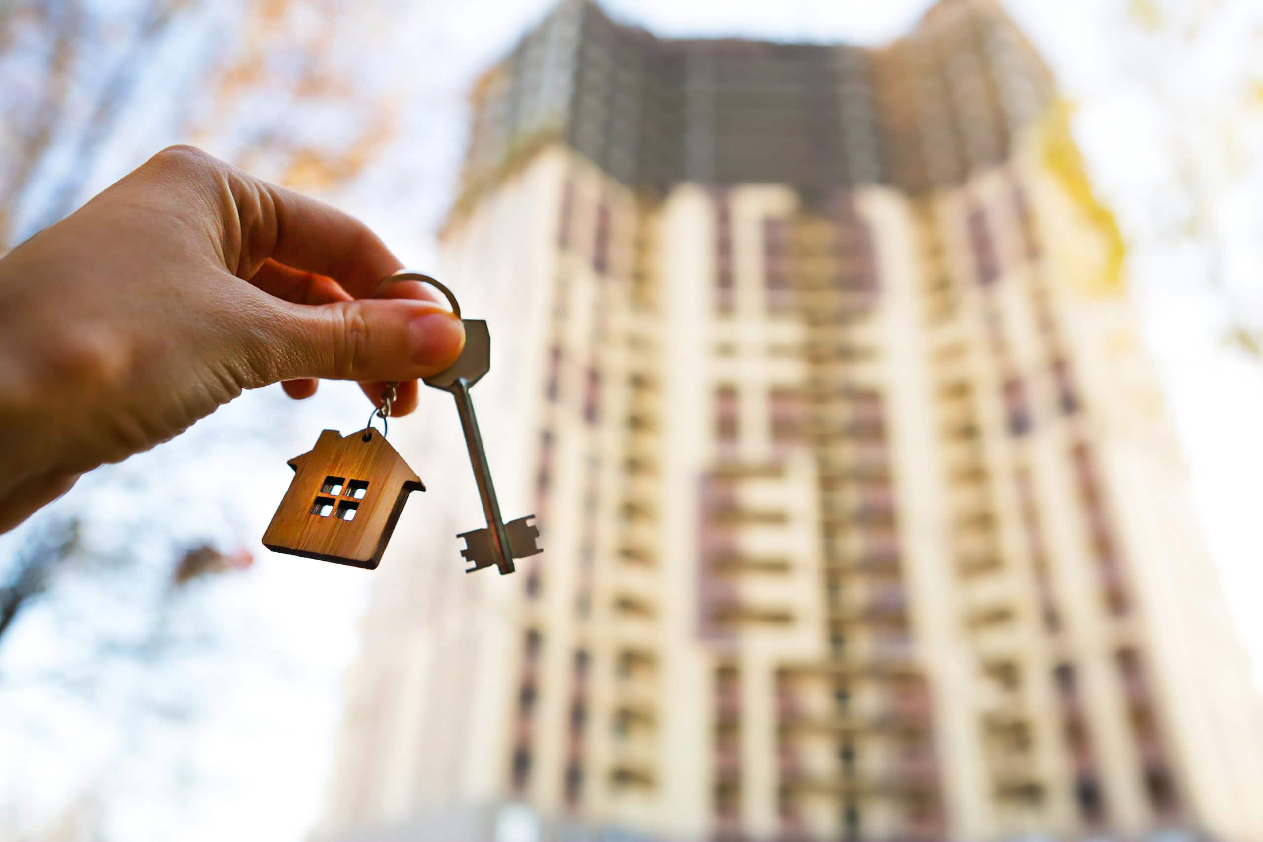 Chiave in mano con simbolo di casa, sfondo di un edificio in costruzione, rappresenta il concetto di acquisto o investimento immobiliare, sicurezza e proprietà edilizia.
