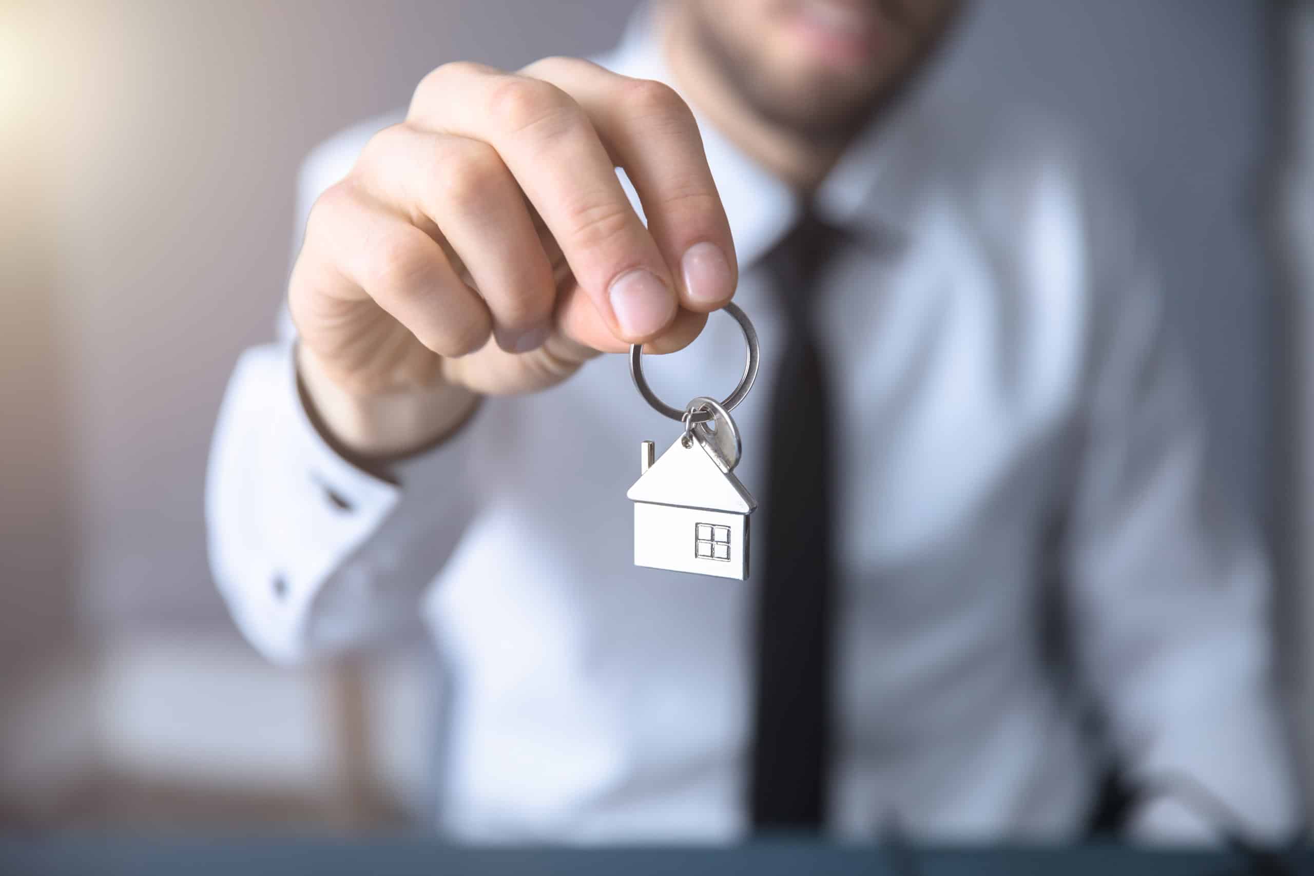 Proprietario che tiene una chiave con una casa in miniatura, simbolo di vendita o affitto immobiliare, rappresentando servizi di intermediazione immobiliare e gestione case.
