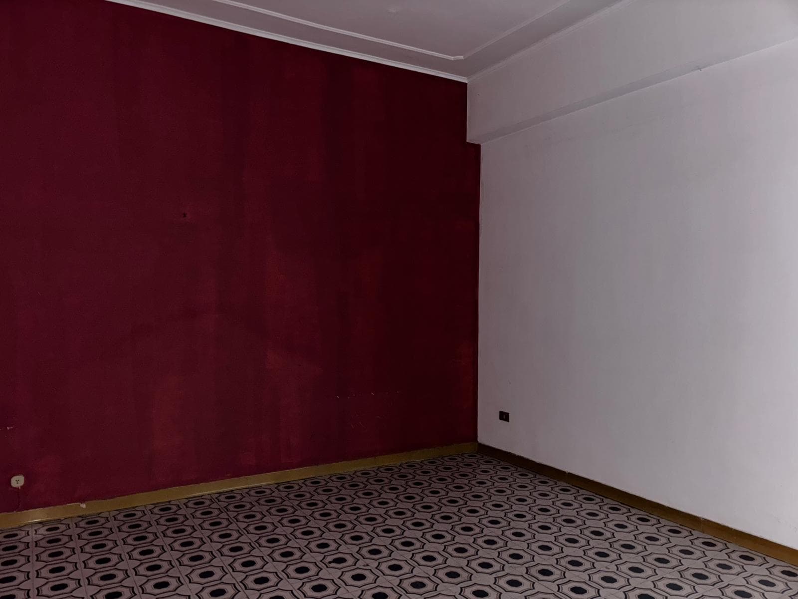 Muro rosso e parete bianca in una stanza vuota con pavimento decorato in piastrelle geometriche.