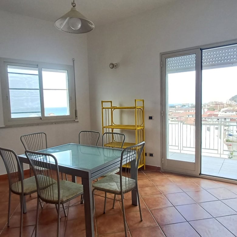 Ampia sala da pranzo con tavolo in vetro e sedie, luminosa e moderna, con accesso a balcone con vista sulla città, ideale per vivere in un ambiente confortevole e funzionale.