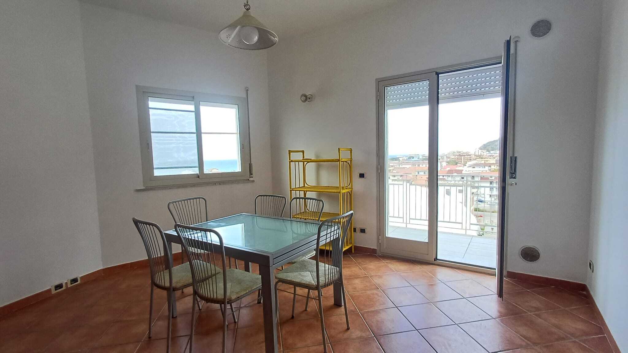 Ampia sala da pranzo con tavolo in vetro e sedie, luminosa e moderna, con accesso a balcone con vista sulla città, ideale per vivere in un ambiente confortevole e funzionale.