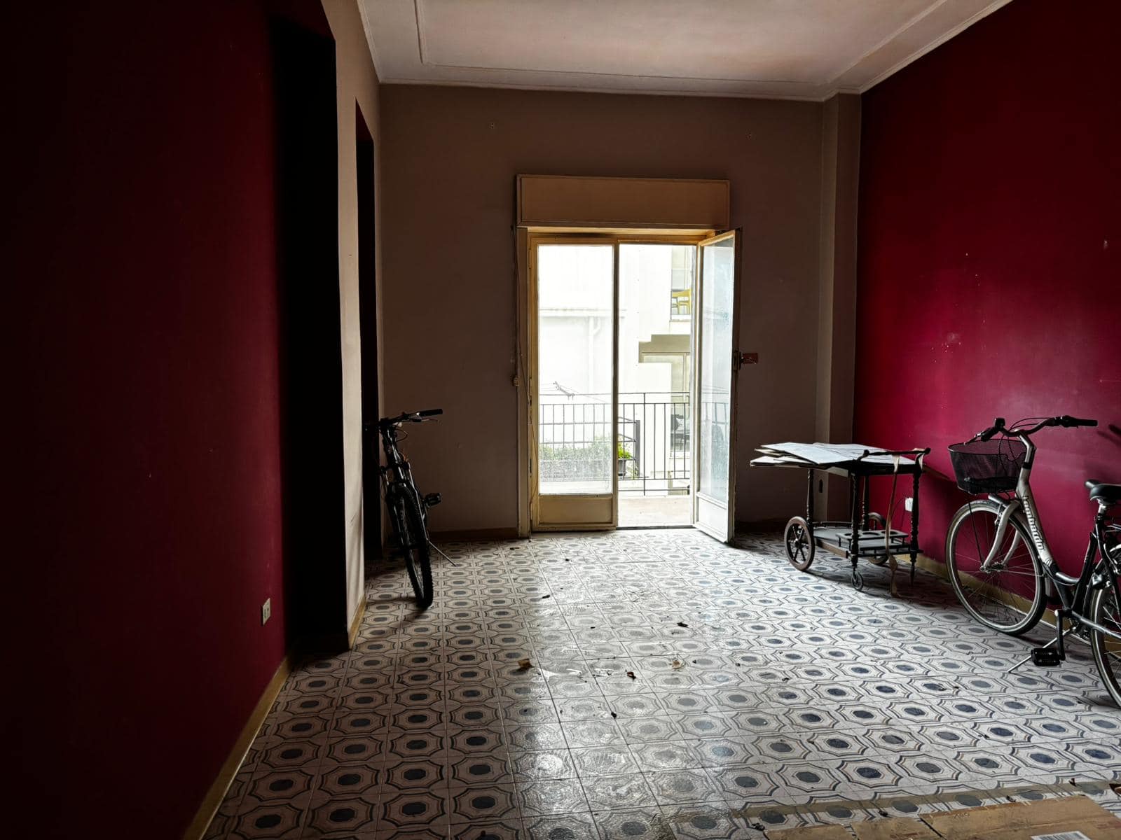 Interno di un appartamento con pareti rosse, biciclette e porta finestra che dà su un balcone, ambiente luminoso e spazioso, ideale per vivere e rilassarsi.