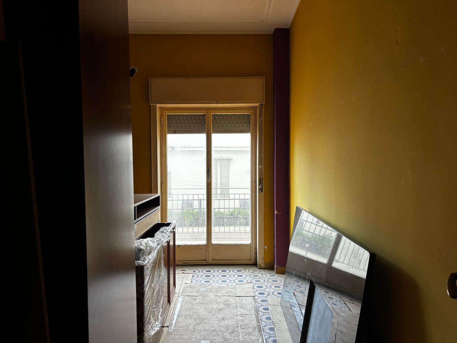 Ampio soggiorno con pareti colorate, grande finestra con vista su balcone e pavimento in piastrelle decorative, arredamento moderno e luminoso.