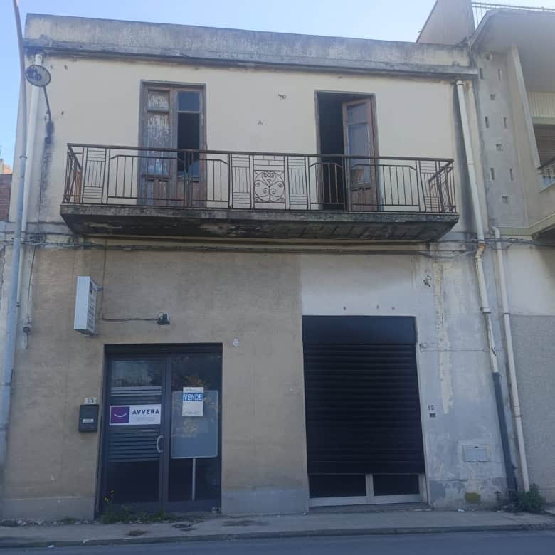 Balcone in ferro battuto su edificio storico in centro città, con finestre e porta d'ingresso al piano terra, in un contesto urbano con edifici residenziali e commerciali.
