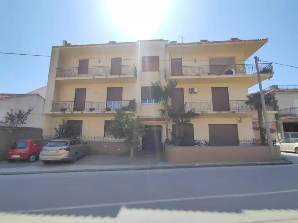 Appartamento residenziale a tre piani con balconi e parcheggio esterno, situato in zona urbana soleggiata, con facciata gialla e accesso principale centrale.