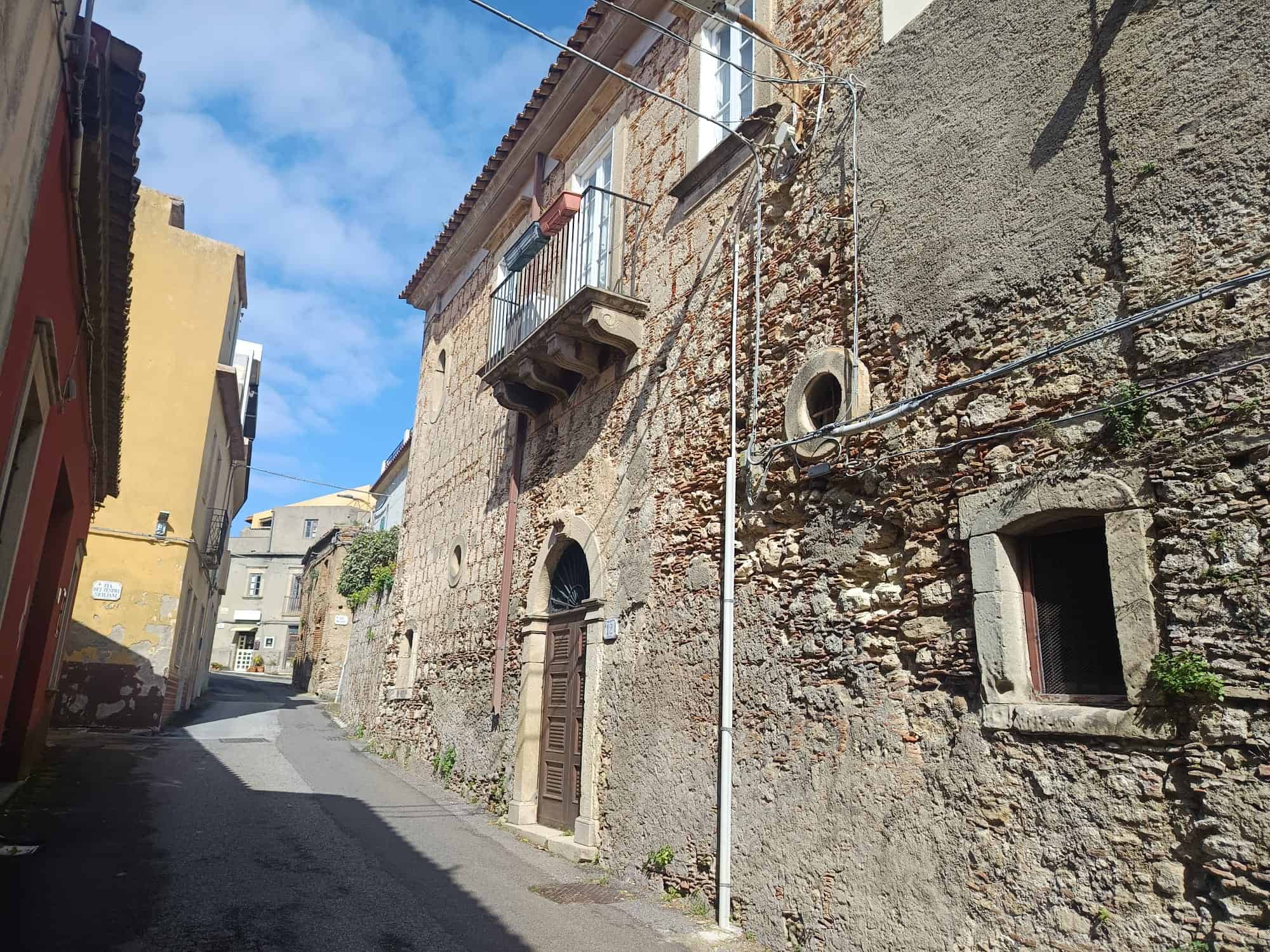 Antic house in a narrow street with stone walls and small windows, typical of historic Italian architecture.
