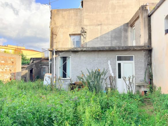 Veranda di una casa in stile rustico con giardino verde e piante, vista esterna di un'abitazione in zona urbana, con pareti in pietra e finestre moderne, ambiente tranquillo e naturale.