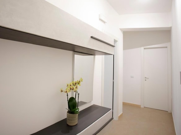 Lavagna a specchio moderna con mensola e pianta di orchidea gialla, ingresso di un appartamento minimalista, pareti bianche e design elegante.