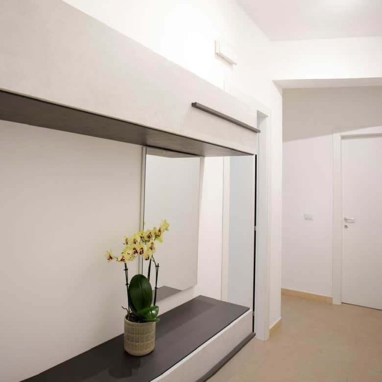 Lavagna a specchio moderna con mensola e pianta di orchidea gialla, ingresso di un appartamento minimalista, pareti bianche e design elegante.