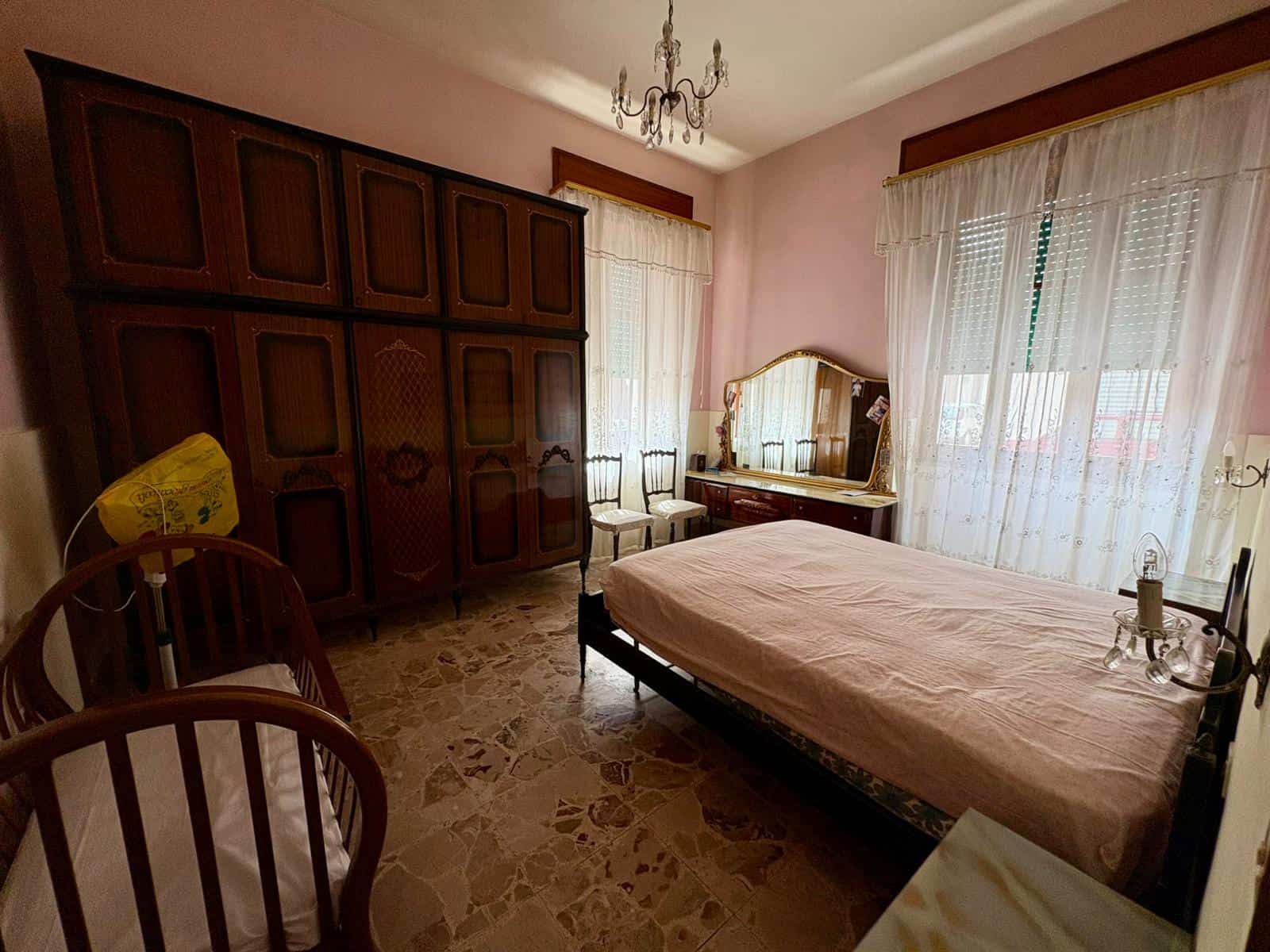 Camera da letto spaziosa con armadio a muro, letto singolo, specchio antico e tende leggere, ambiente luminoso e accogliente.