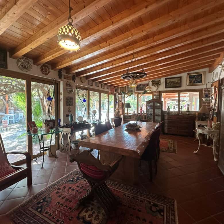 Pannello di vetro con vista sul giardino e arredamento rustico in soggiorno con tavolo in legno, sedie e decorazioni vintage, ambiente accogliente e luminoso.