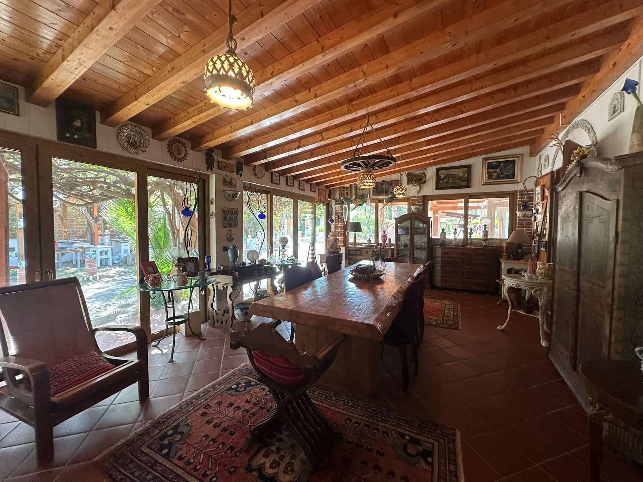 Pannello di vetro con vista sul giardino e arredamento rustico in soggiorno con tavolo in legno, sedie e decorazioni vintage, ambiente accogliente e luminoso.
