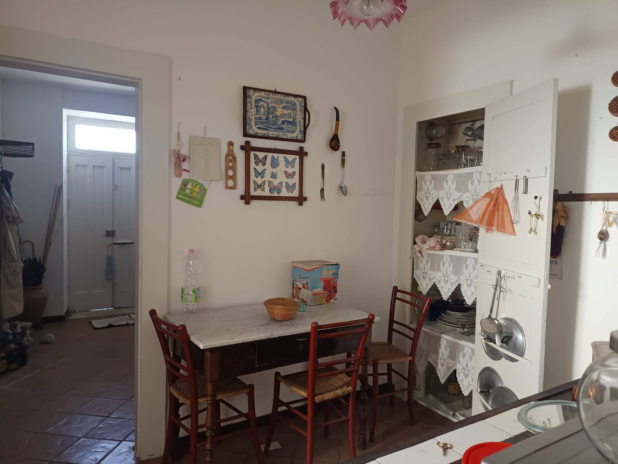 L'immagine mostra una zona pranzo in stile rustico con un tavolo in legno e sedie abbinate, decorazioni vintage e oggetti artigianali, creando un ambiente accogliente e familiare.