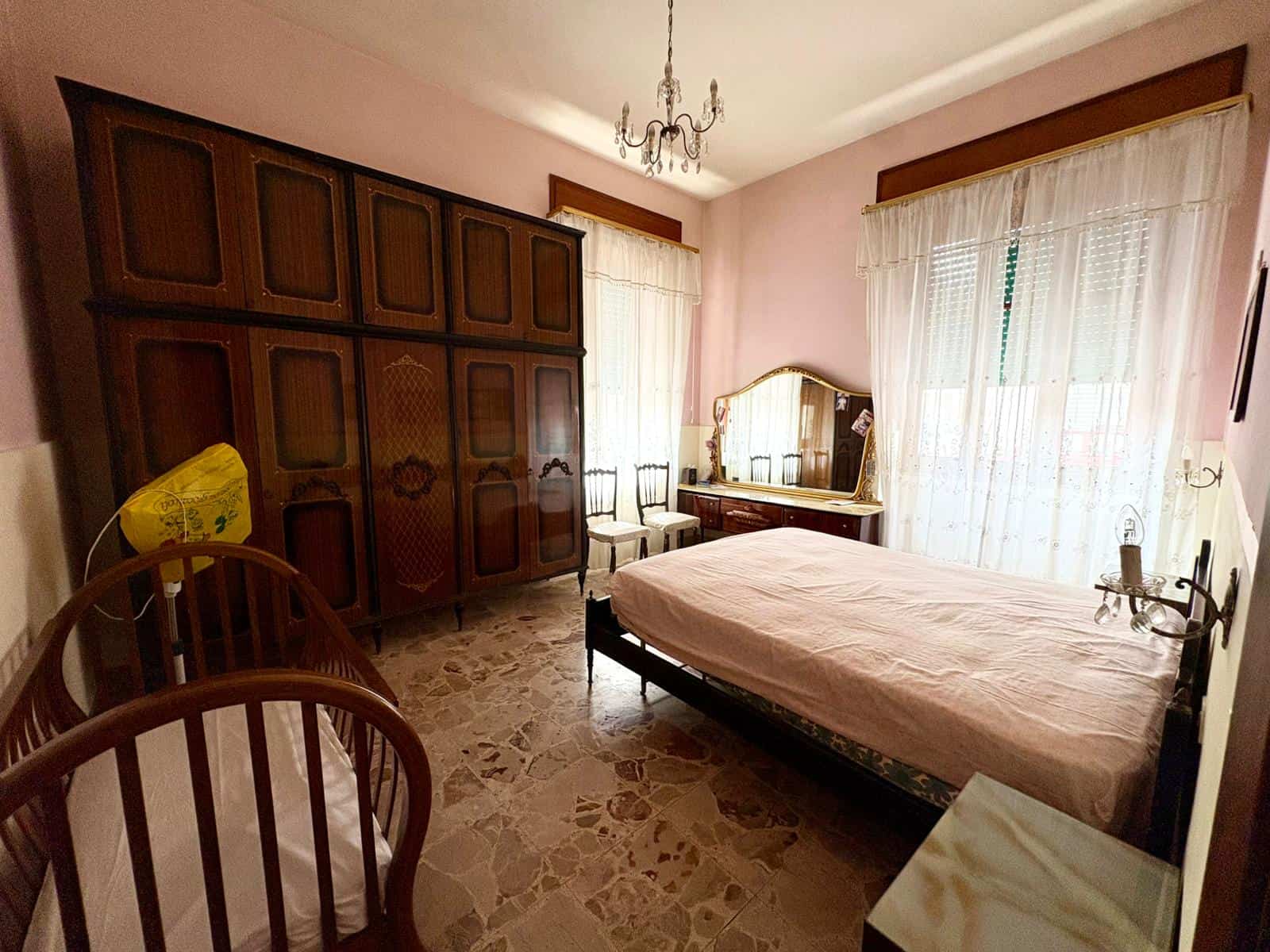 Una stanza da letto spaziosa con mobili in legno, grande armadio e finestra con tende leggere, ambiente accogliente e luminoso, ideale per la vendita o l'affitto di immobili residenziali.