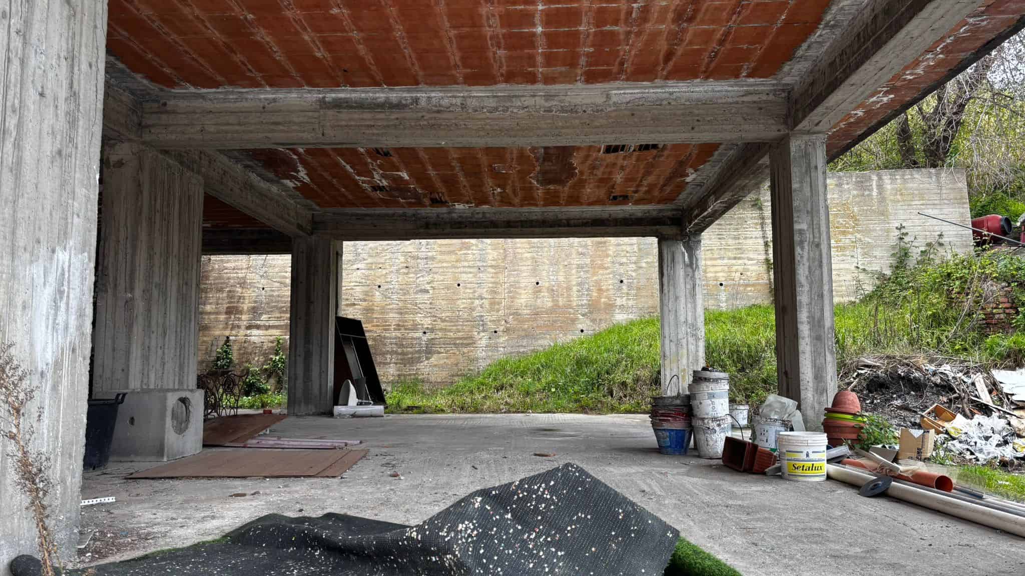 Ampio garage in costruzione con struttura in cemento e mattoni, spazio per parcheggio e deposito, ambiente industriale e moderno, pronto per finiture interne.
