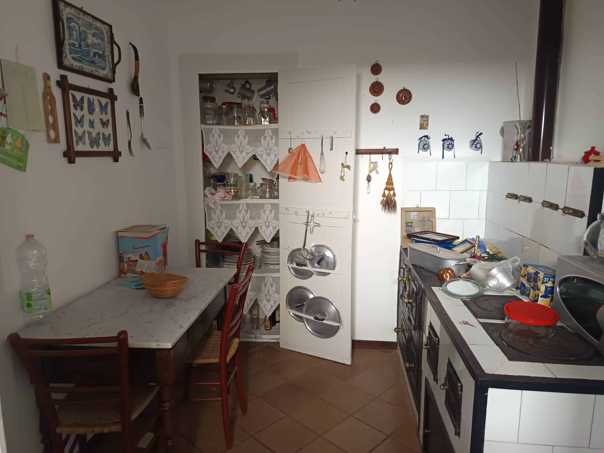 Cucina compatta e accogliente con mobili bianchi, utensili e decorazioni tradizionali, ideale per ambienti domestici italiani.