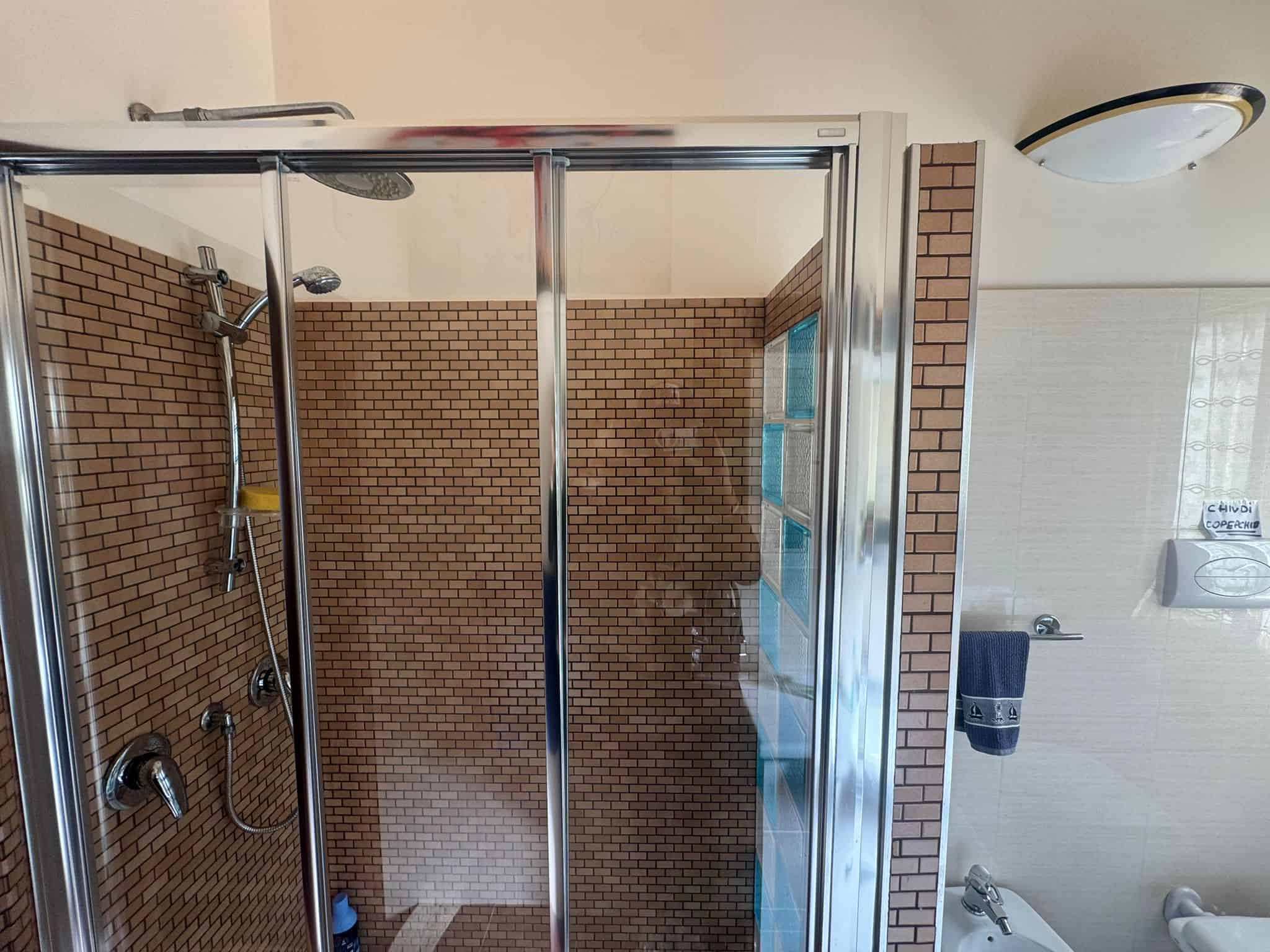 Doccia moderna con pareti in vetro e piastrelle marroni, ideale per bagni eleganti e funzionali.