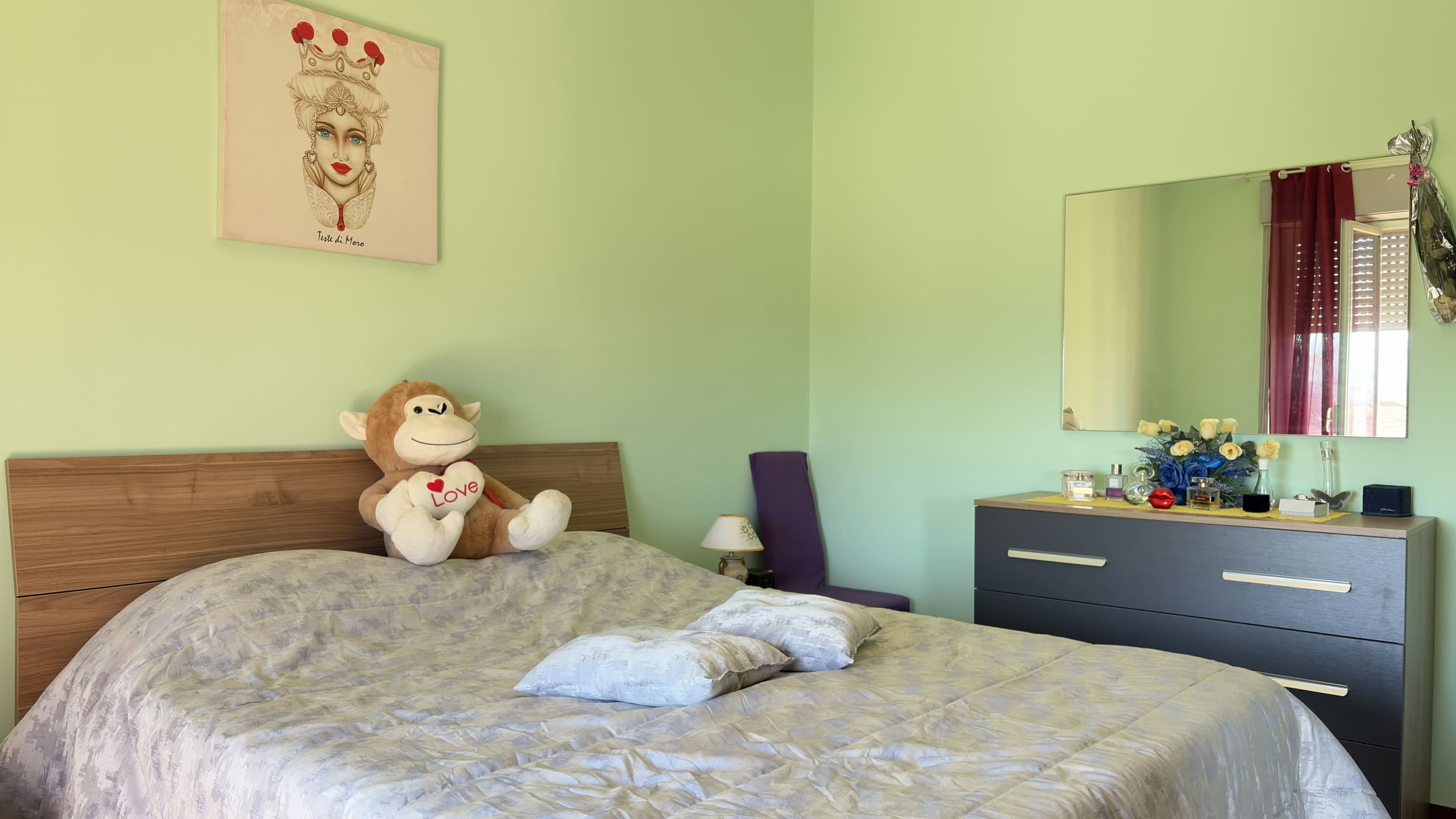 Letto matrimoniale con cuscini e peluche in camera da letto luminosa, decorata con arte moderna e mobili eleganti, ideale per case in vendita o affitto.