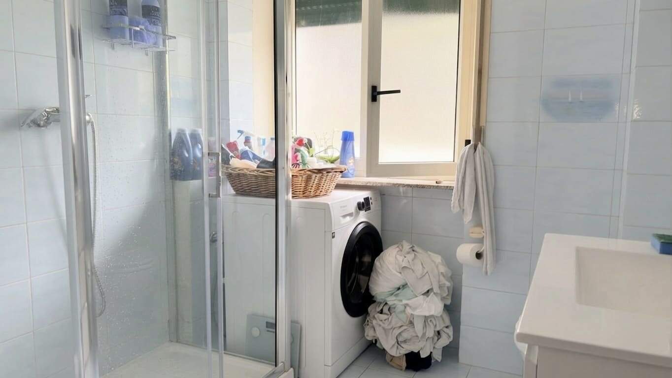 Lavatrice in un bagno con finestra, asciugamani e prodotti per la pulizia, ambiente luminoso e funzionale.