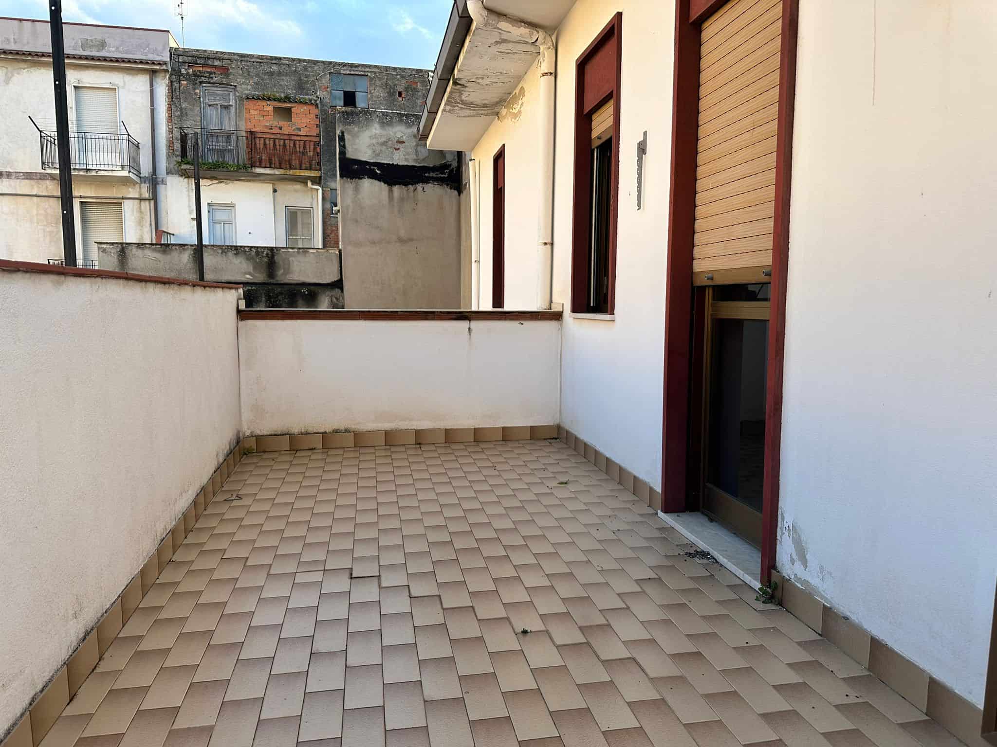 Ampio balcone con pavimentazione in piastrelle beige, vista su edifici residenziali, ideale per relax e momenti all'aperto, in zona urbana tranquilla.