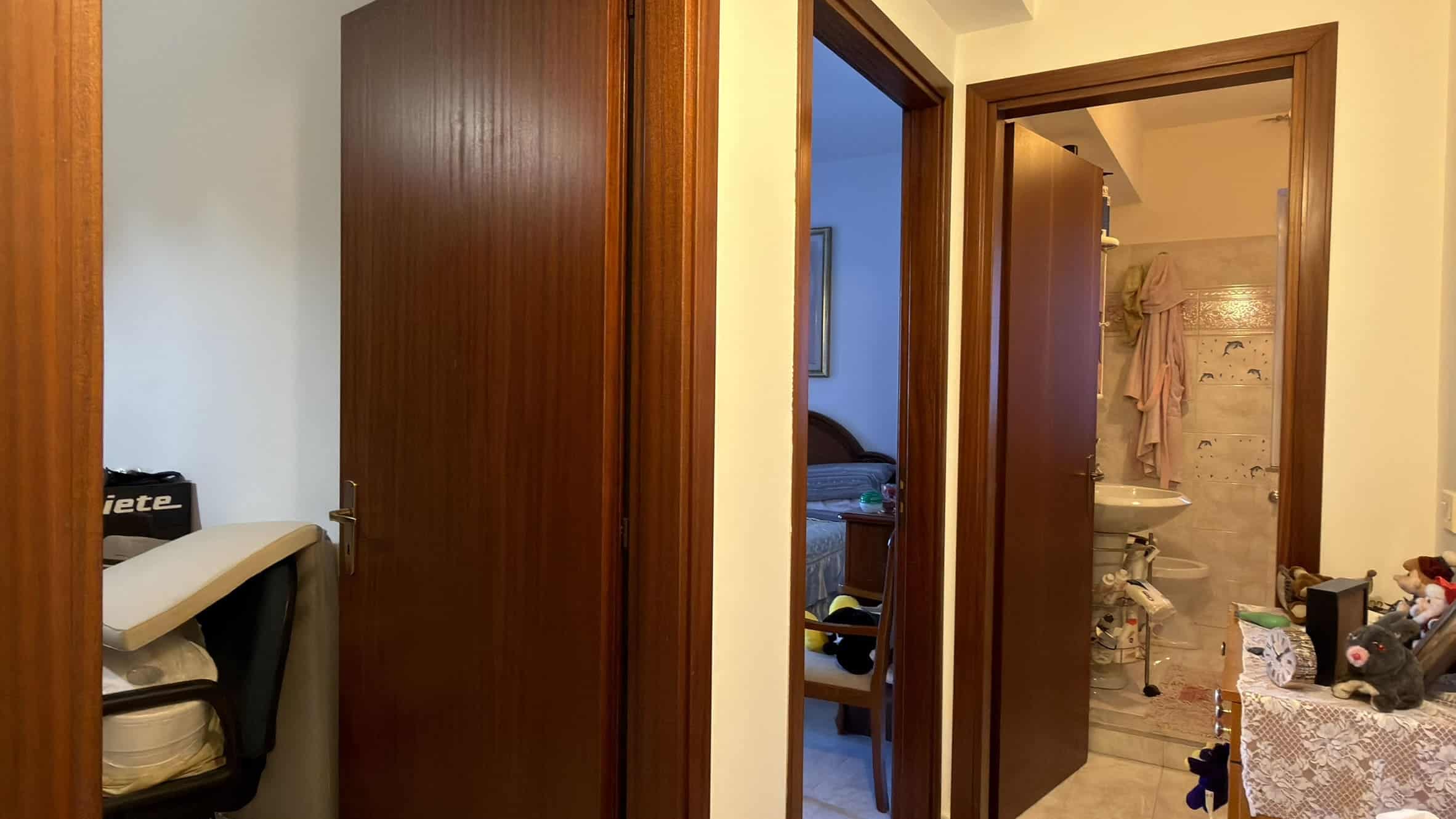 Ampia vista di un ingresso con porte in legno, che conduce a camere da letto e bagno, in un appartamento moderno e ben arredato, ideale per chi cerca soluzioni abitative di qualità.