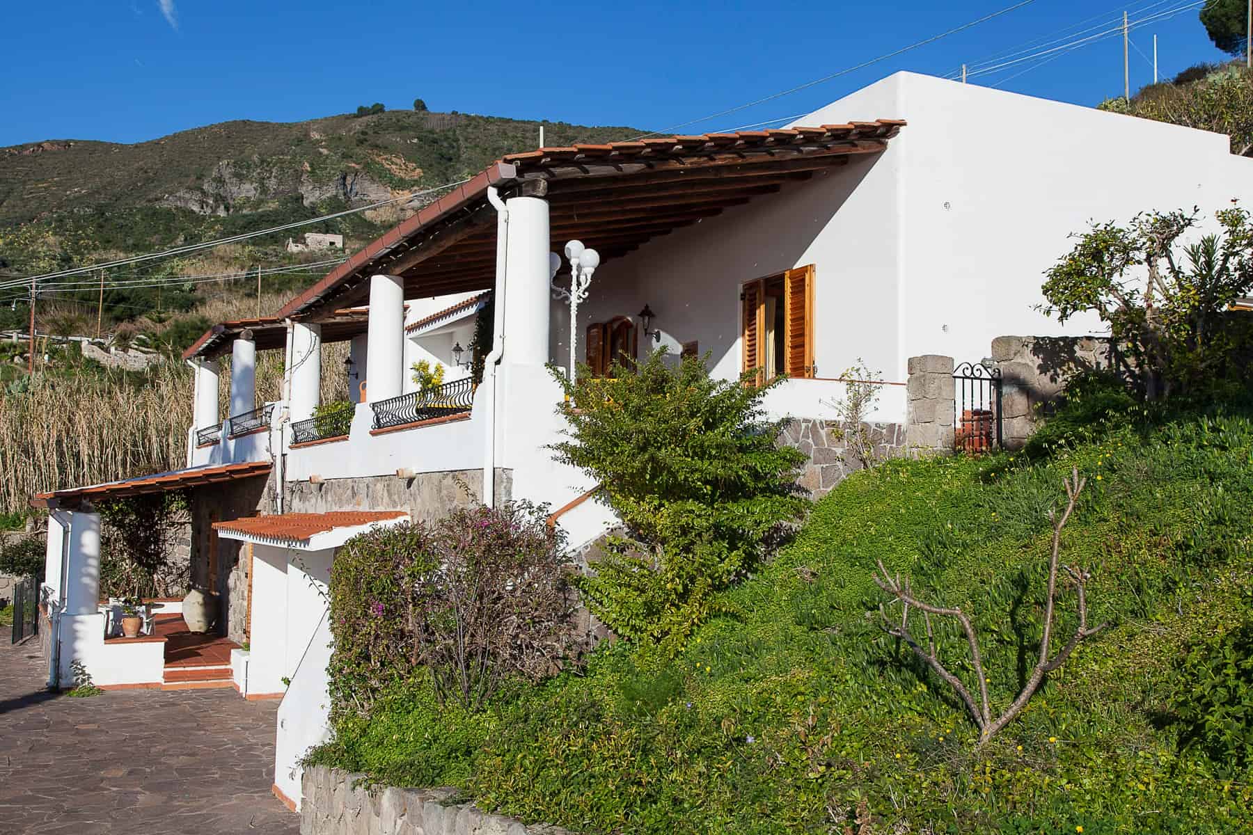 Villa in stile mediterraneo con facciata bianca, terrazza panoramica e giardino curato, immersa nella natura con vista sulle colline. Ideale per vacanze rilassanti e soggiorni in tranquillità.