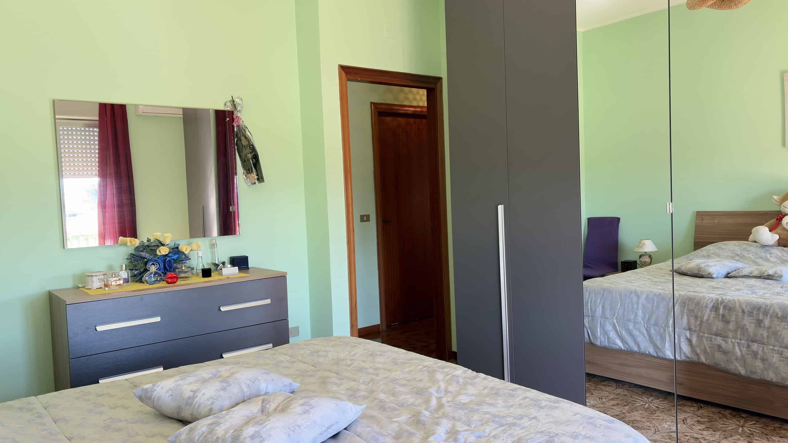 Spazio camera da letto con armadio a specchio, letto matrimoniale e mobili moderni in ambiente luminoso e accogliente.