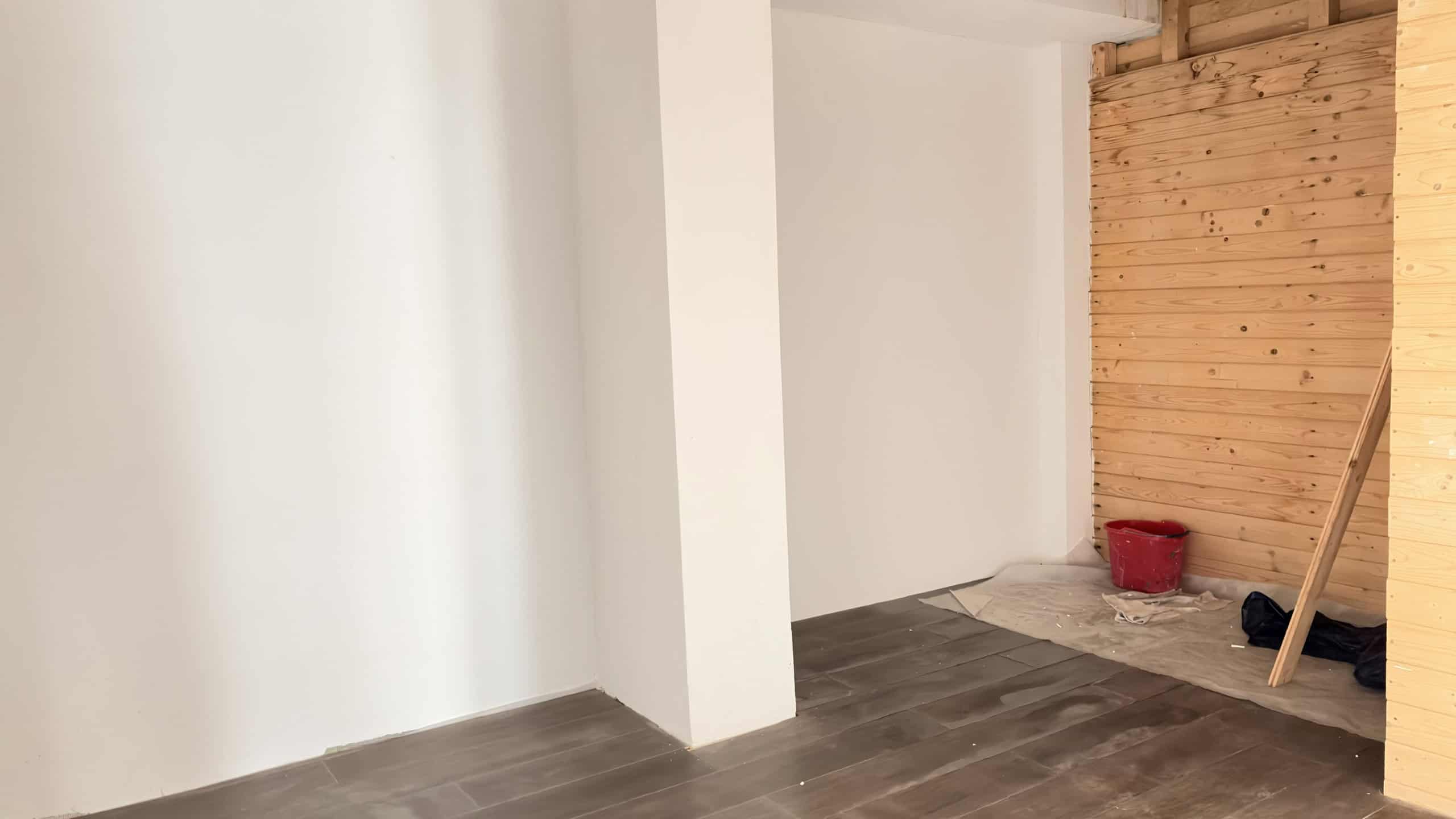 Spazio interno di una casa in fase di ristrutturazione con pareti bianche, pavimento in gres effetto legno e parete in legno naturale, pronto per essere arredato e personalizzato.