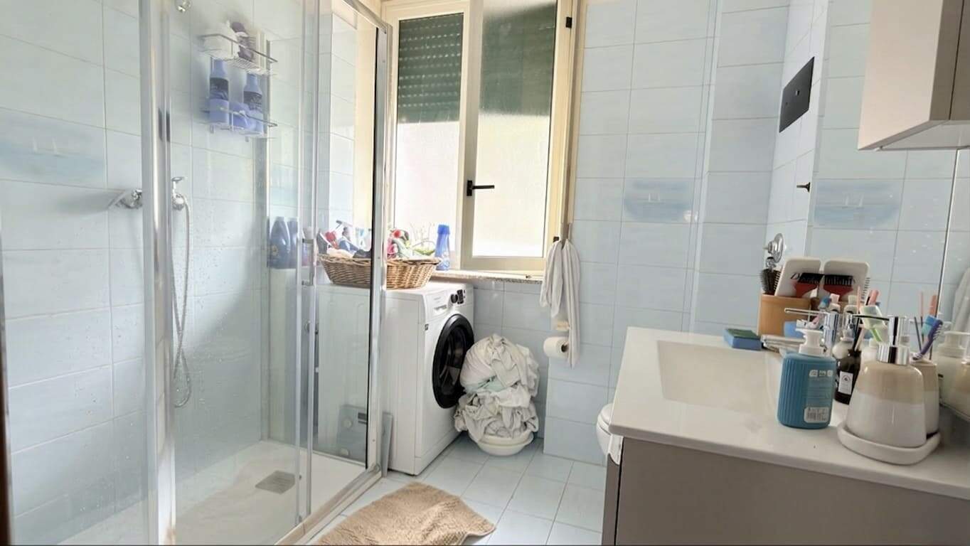 Lavatrice e bagno con doccia, ambiente luminoso e funzionale, ideale per la cura personale e il comfort quotidiano. Spazio ben organizzato con accessori e prodotti per l'igiene.