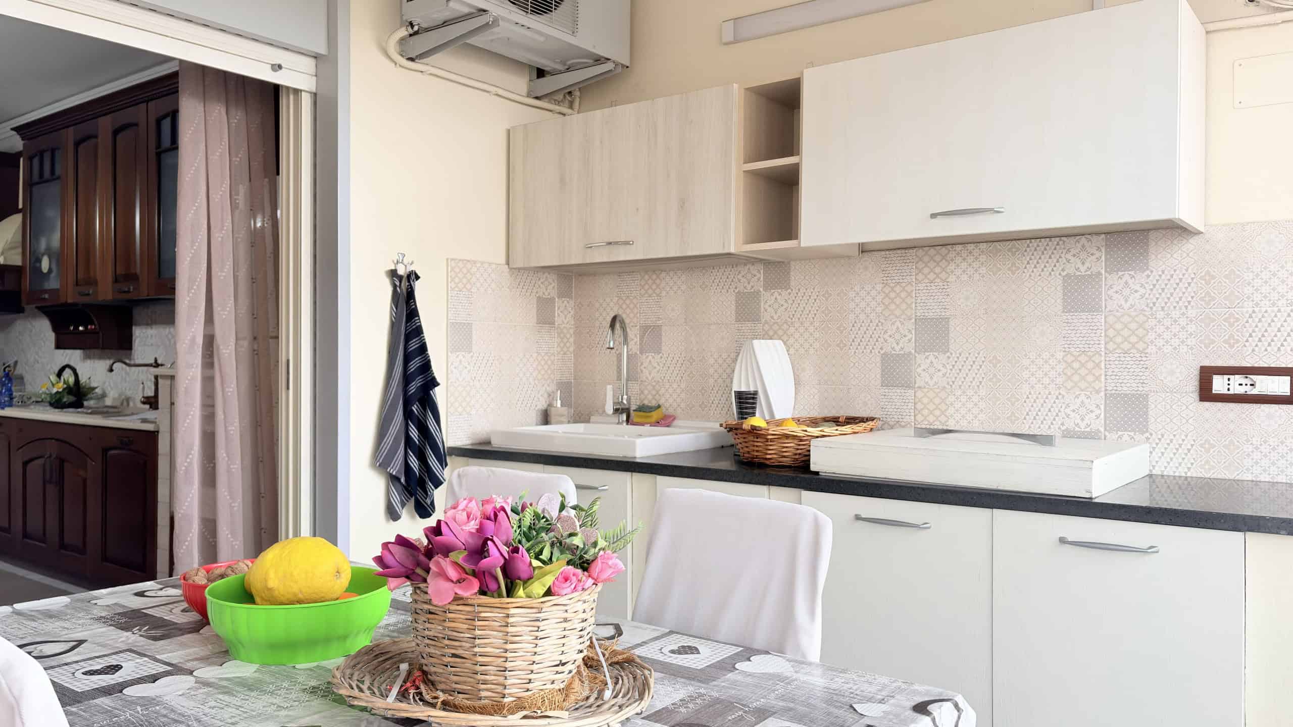 Lavagna di cucina moderna con mobili bianchi, piano di lavoro in superficie chiara, decorazioni floreali e accessori pratici, ideale per case in stile contemporaneo.