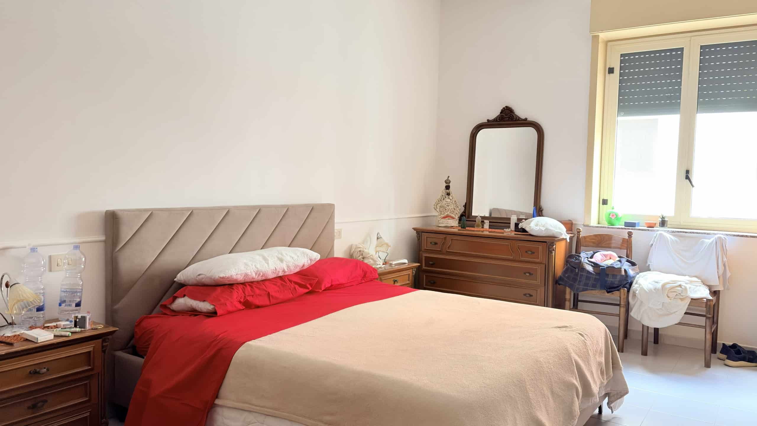 Letto matrimoniale con testiera imbottita in tessuto beige, in una camera da letto luminosa e accogliente.