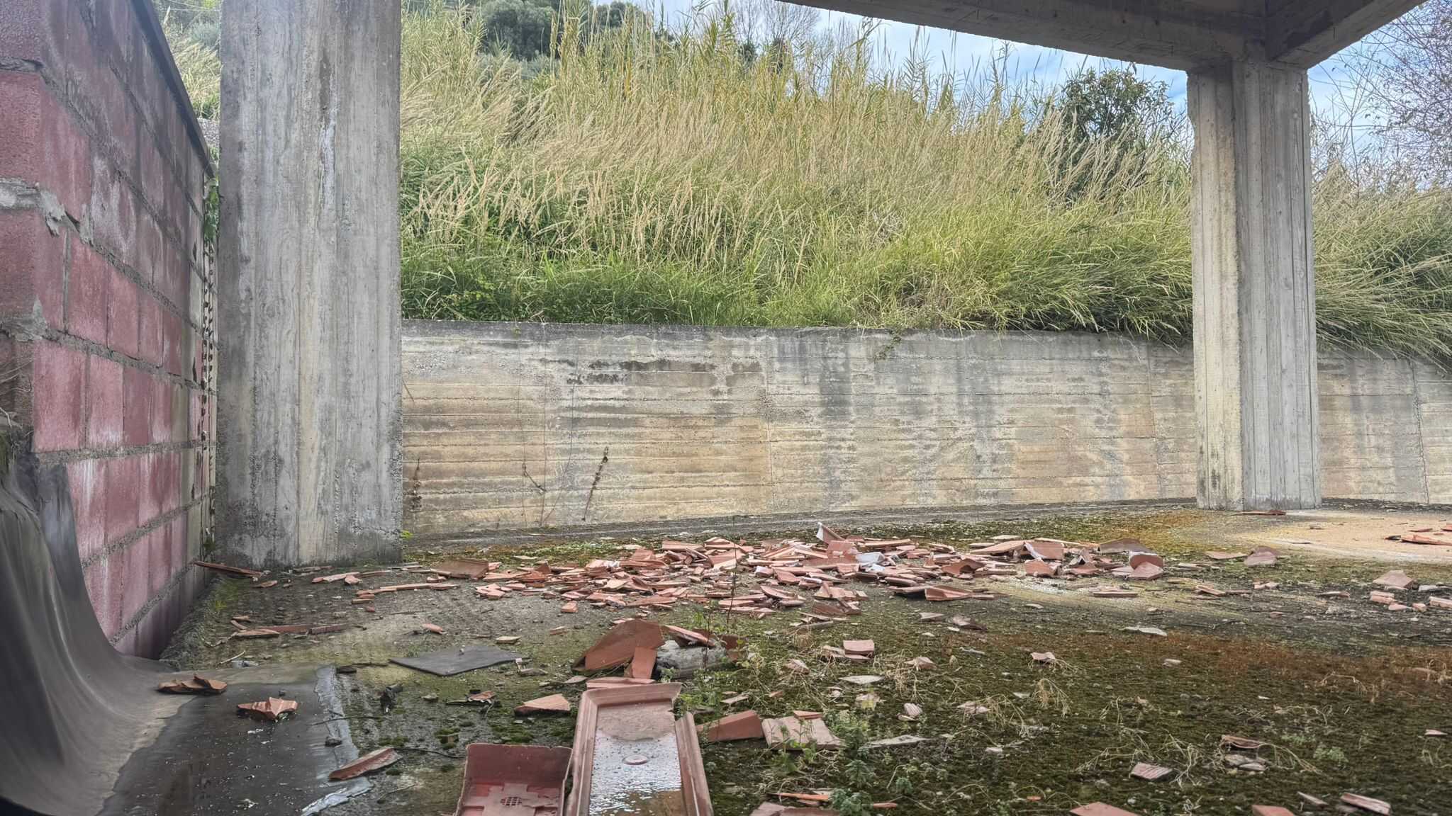 Scorcio di un'area sottostante un ponte con terreno ricoperto di detriti e mattoni rotti, circondata da vegetazione naturale e strutture in cemento. Ideale per analisi di ambienti urbani e infrastrutt.